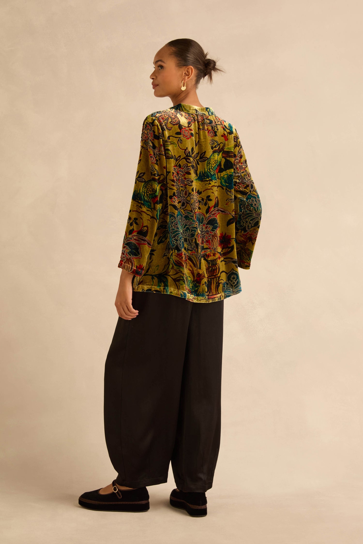 A person standing in profile wearing an olive green Silk Velvet Floral Devore Shirt and loose black trousers.