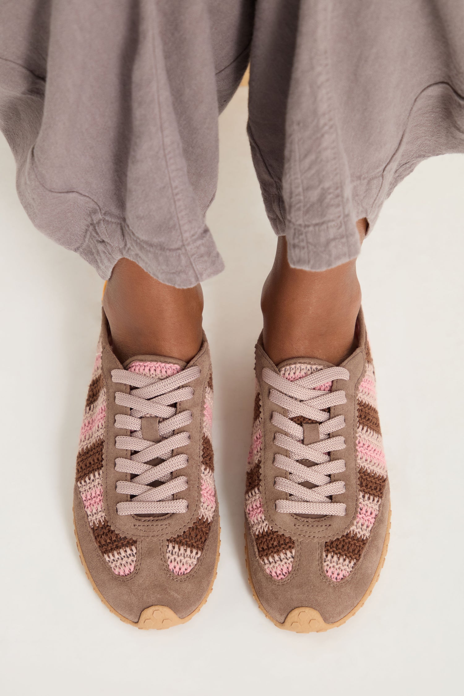 Person wearing taupe wide-leg pants and Bridge Woven Brown Crochet Trainers with cushioned soles, standing on a white surface, viewed from above.