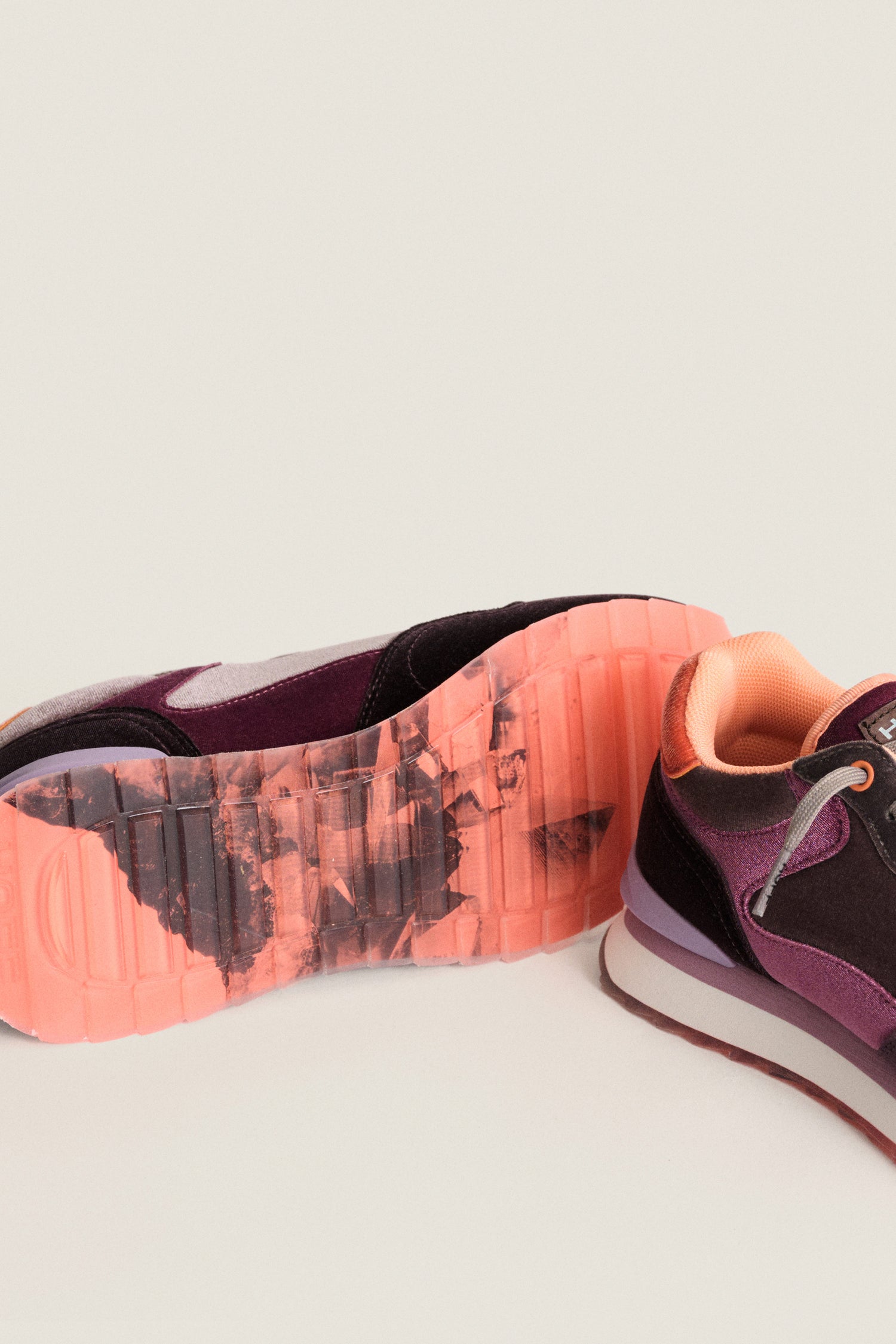 Two Purple City Velvet Trainers in shades of purple and peach, with one on its side displaying a translucent sole featuring a marbled orange and black pattern.