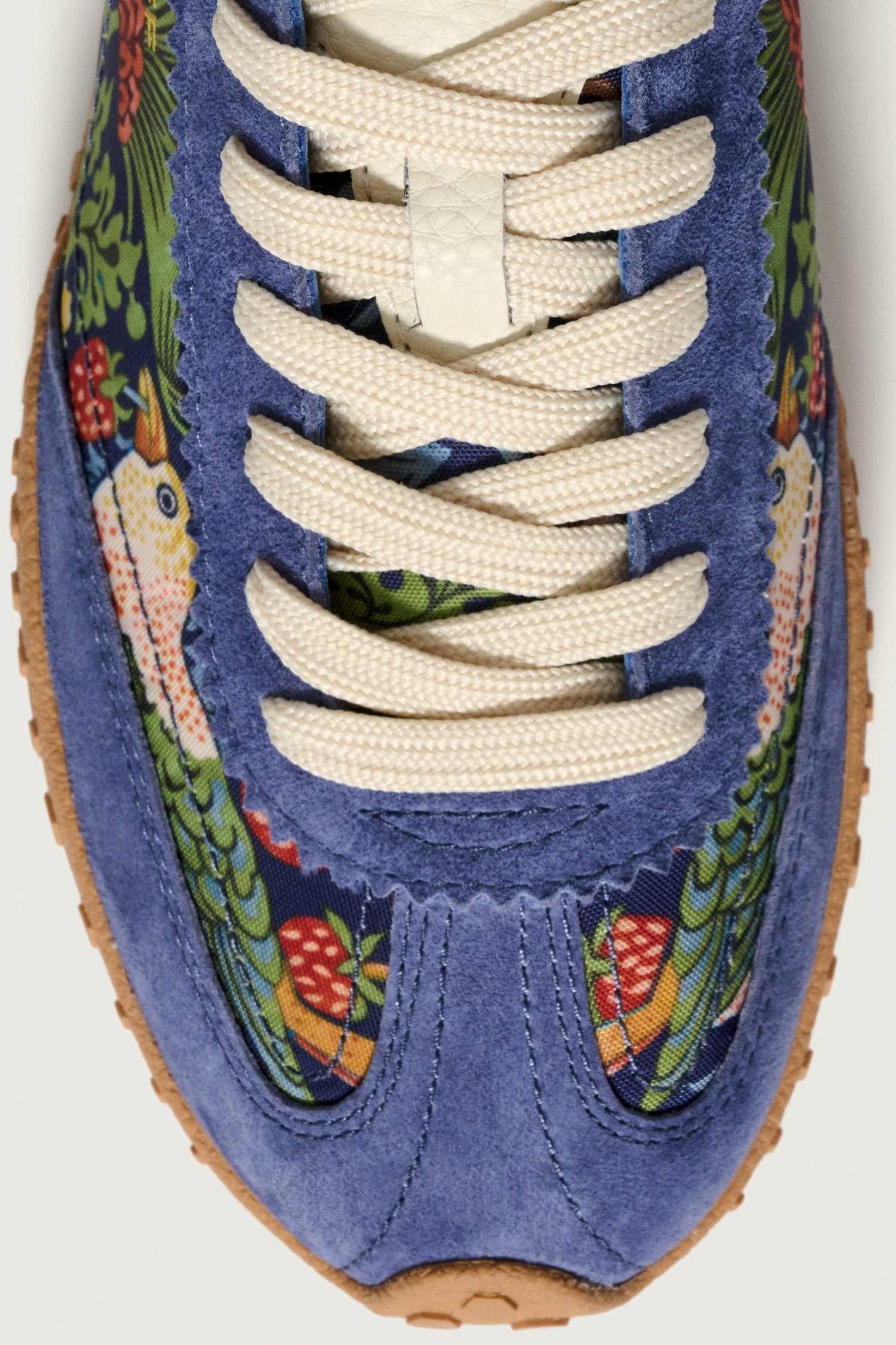 Close-up of Blue William Morris Bridge Trainers featuring cream laces, blue suede accents, a light brown sole, and fabric with a decorative Strawberry Thief print of birds and flowers.
