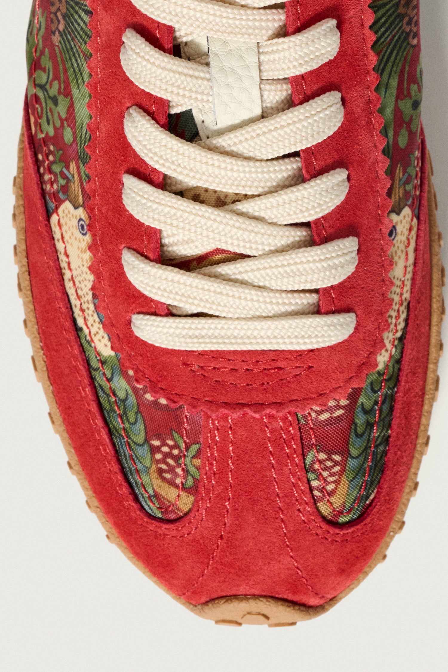 Close-up of the toe and laces of Red William Morris Bridge Trainers, featuring red suede, Strawberry Thief floral fabric, and cream laces with a matching sole.