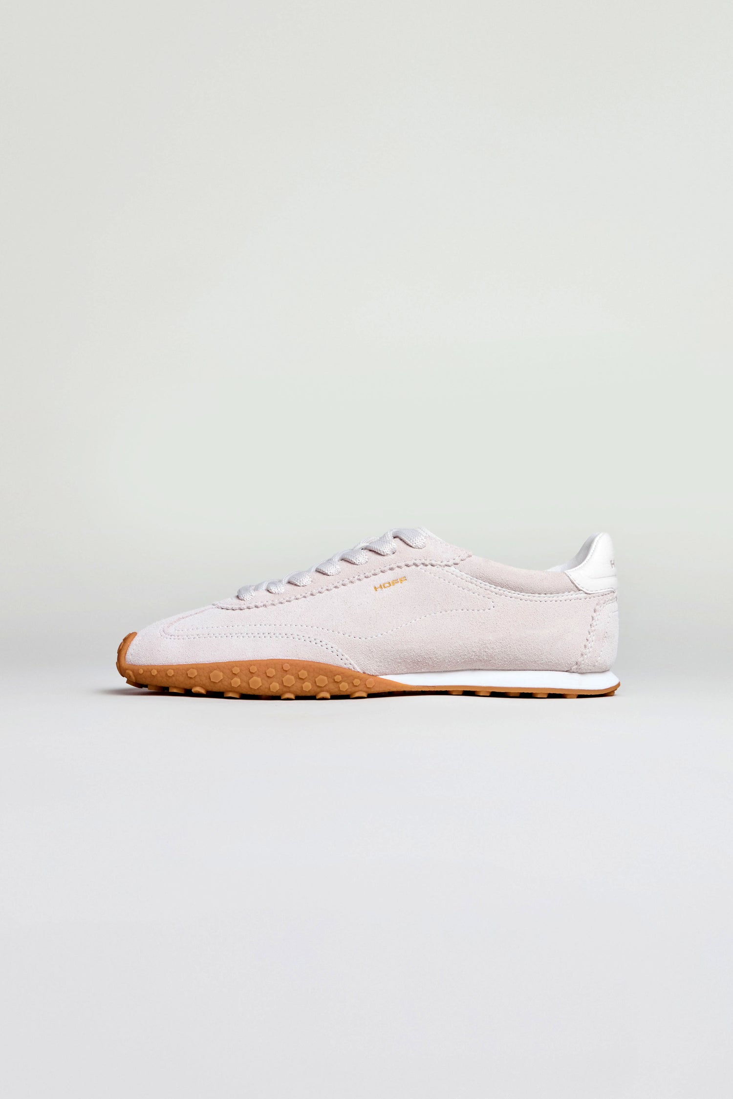 The Bridge Suede Trainers are white athletic sneakers inspired by retro running shoes, featuring a gum rubber sole, side laces, and a low profile, displayed against a plain light background.