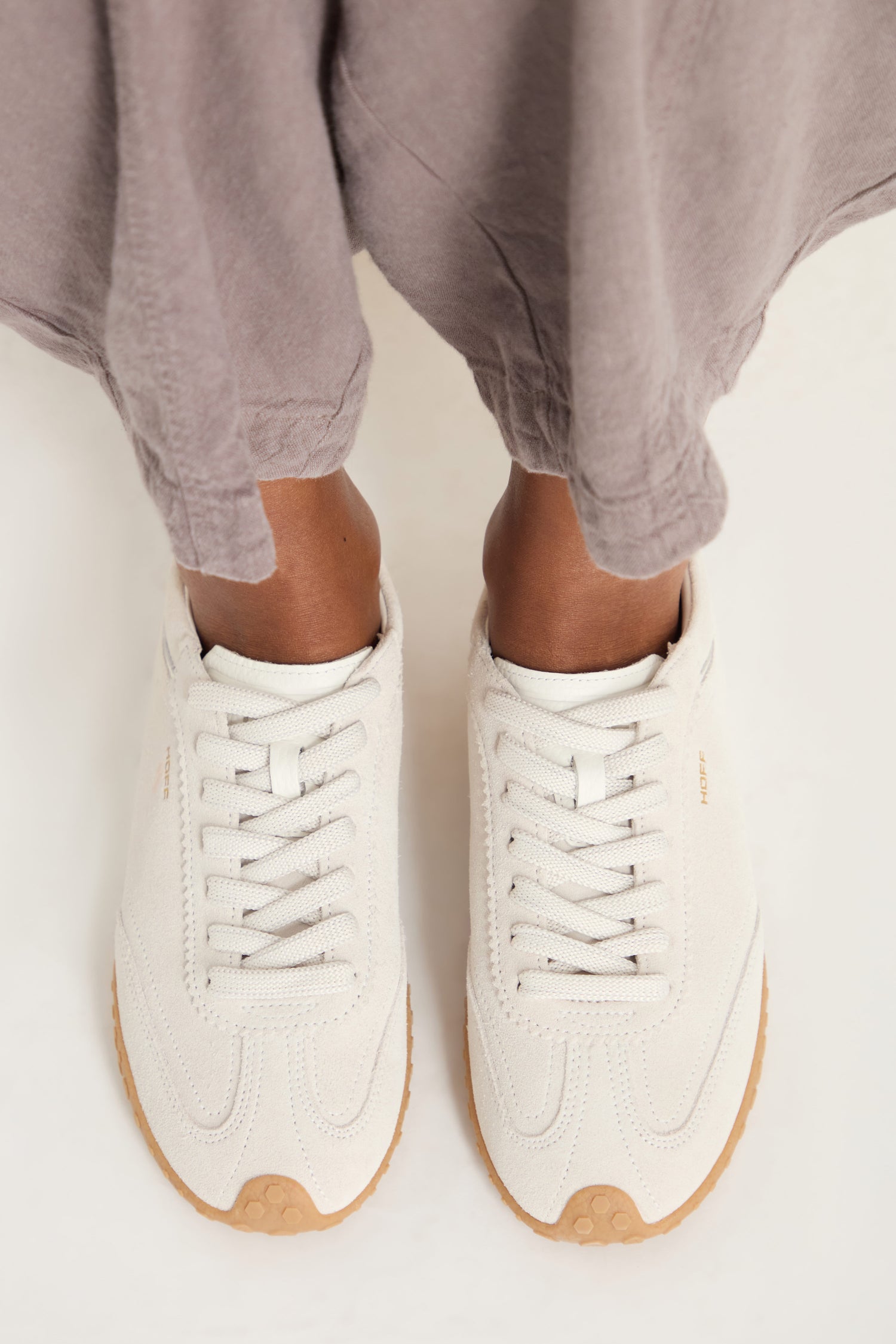 Person wearing Bridge Suede Trainers in a light color with loose grayish pants, viewed from above.