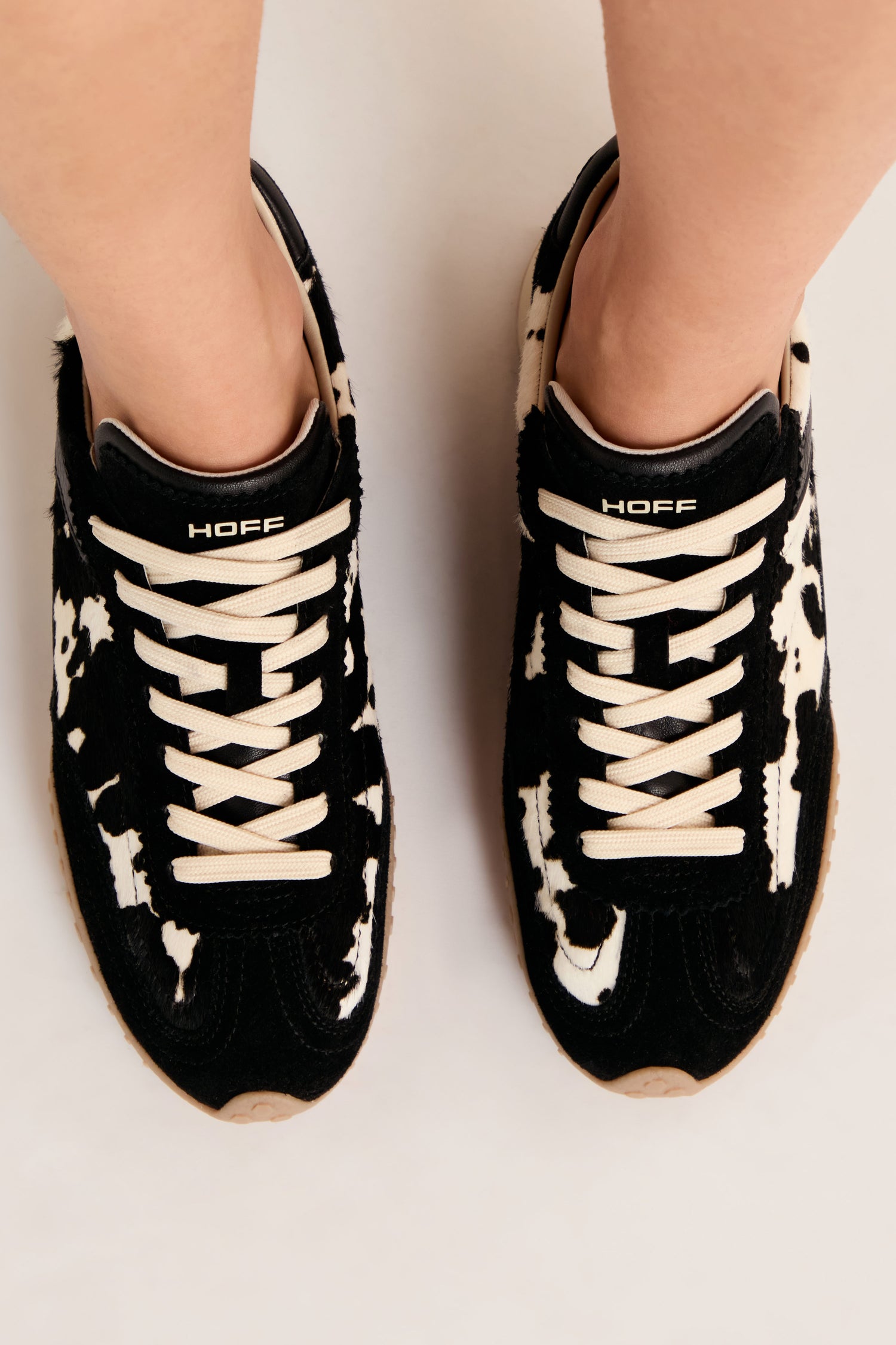 A person wearing Animal Print Bridge Trainers with a cow pattern and “HOFF” branding, viewed from above.