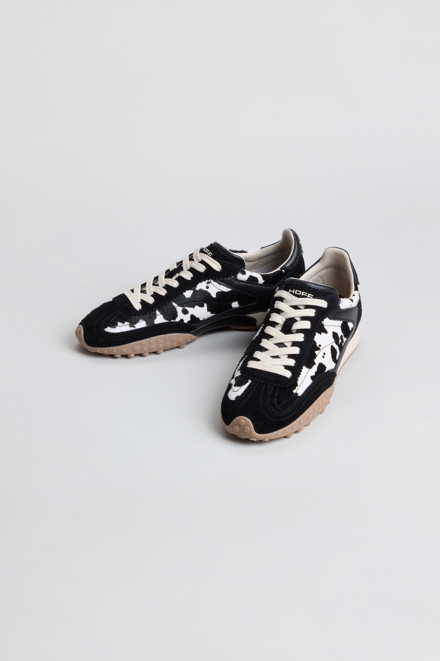A pair of Animal Print Bridge Trainers featuring a black and white camo pattern in low-top suede, beige laces, and tan rubber soles, displayed on a plain light background.