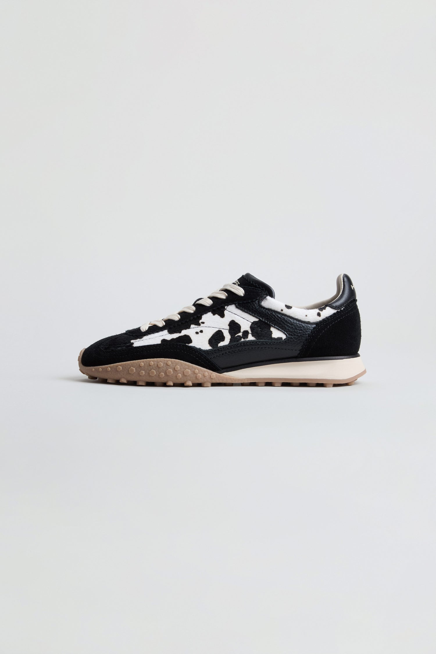 Animal Print Bridge Trainers featuring a black and white cow print pattern, beige sole, and black laces are displayed on a plain white background.