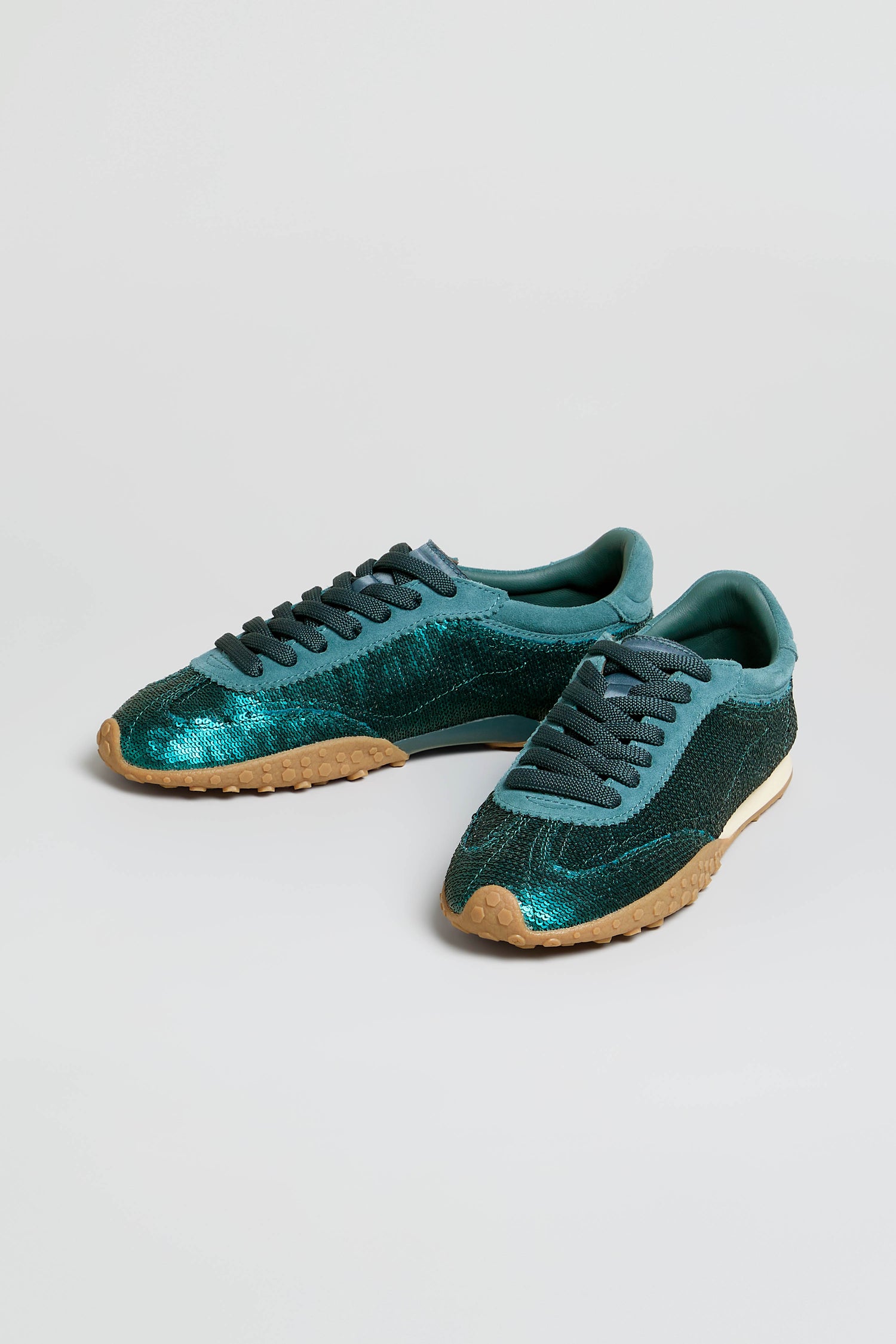 A pair of Sequin Bridge Trainers in teal glitter sequin, featuring dark teal laces, beige rubber soles, and a plush memory-foam insole, displayed on a plain white background.