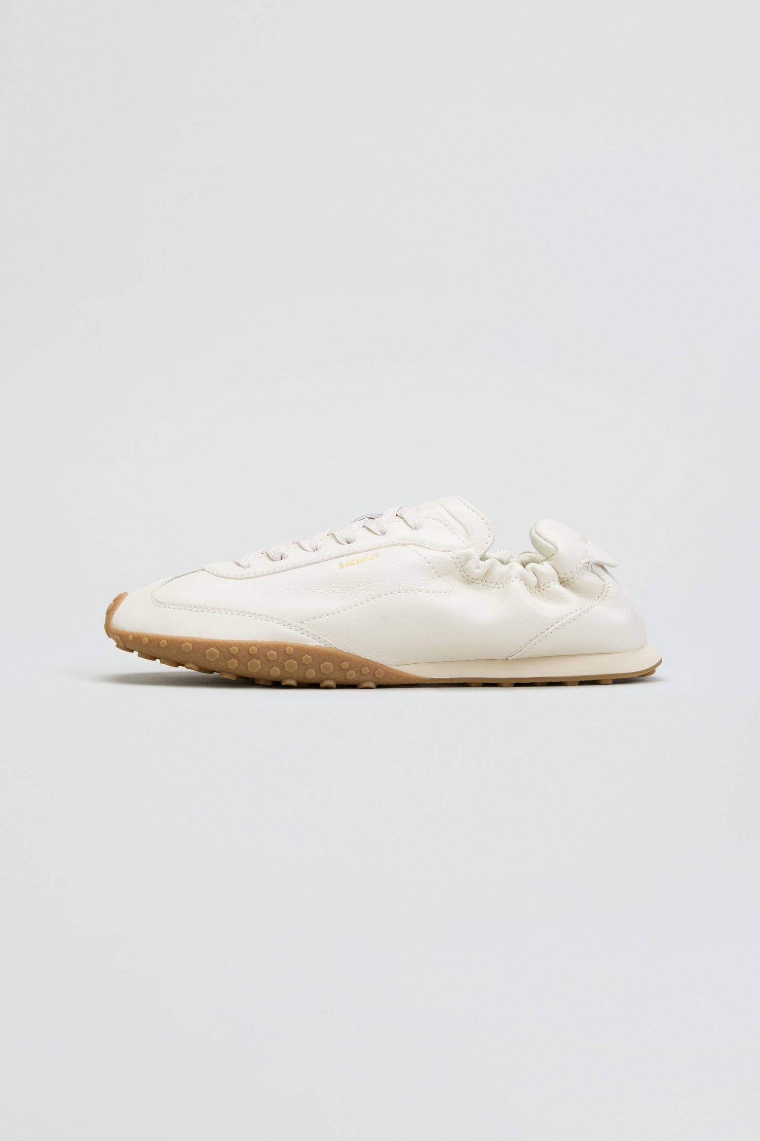 The Napa Leather Bridge Trainers are white low-top sneakers featuring a textured sole, visible stitching, and a subtle elastic accent at the heel. Photographed on a clean light background, these low profile trainers combine comfort and style for everyday wear.
