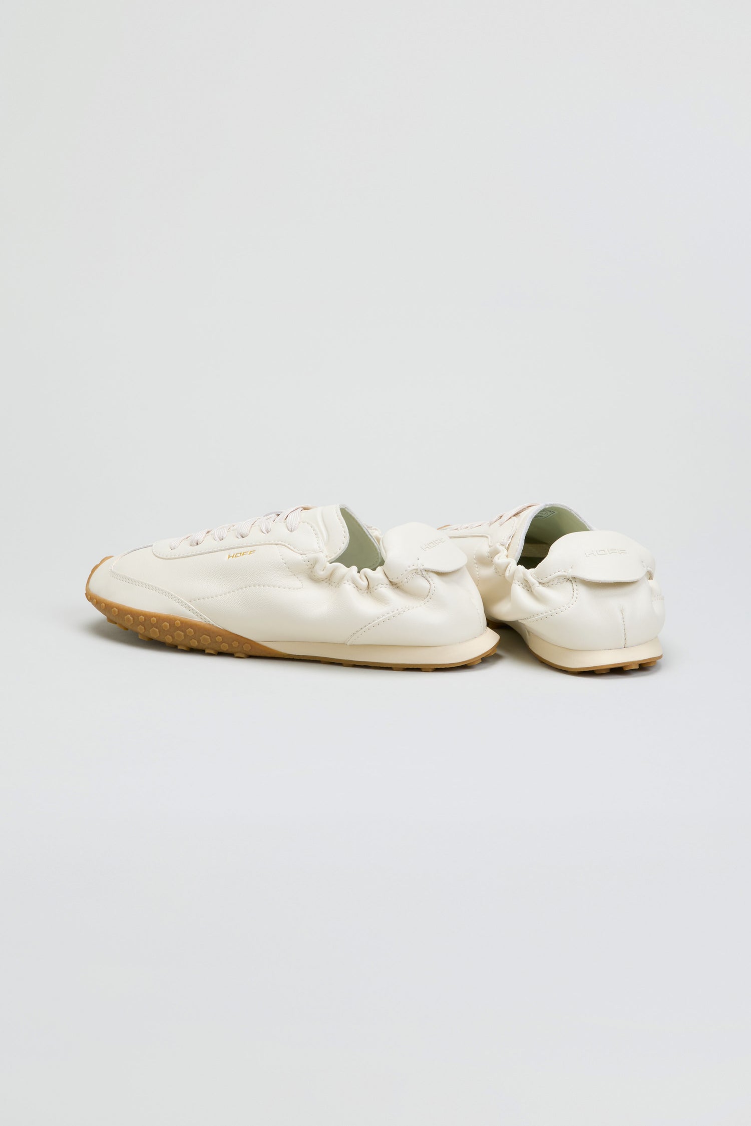 A pair of Napa Leather Bridge Trainers, crafted from cream leather with tan rubber soles in an off-white, low profile design, is placed on a plain white background.