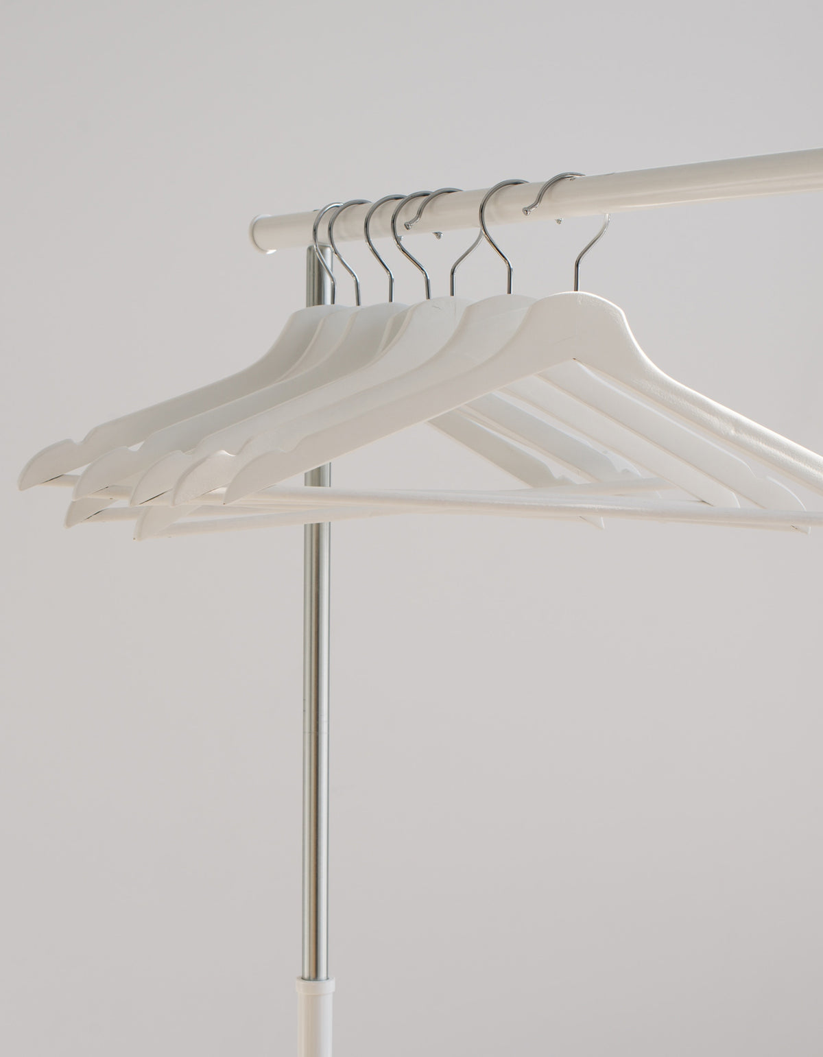 A image of seven white hangers, neatly arranged on a minimalistic white clothing rack against a soft grey background