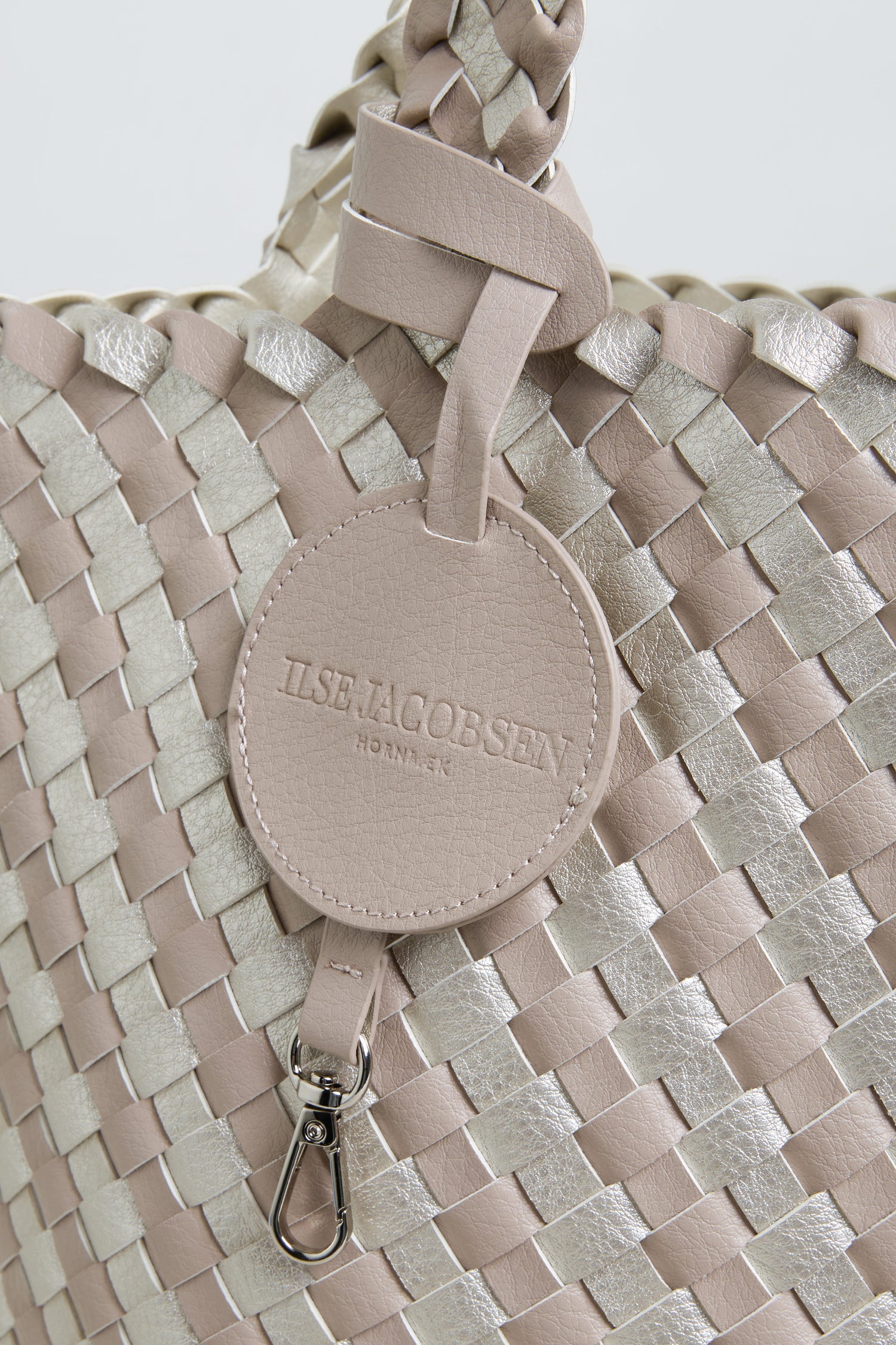 Close-up of the Woven Reversible Grey & Silver Bag, highlighting its basket weave design, round leather tag embossed with "ILSE JACOBSEN HORNBAEK," and a shiny metal clasp.