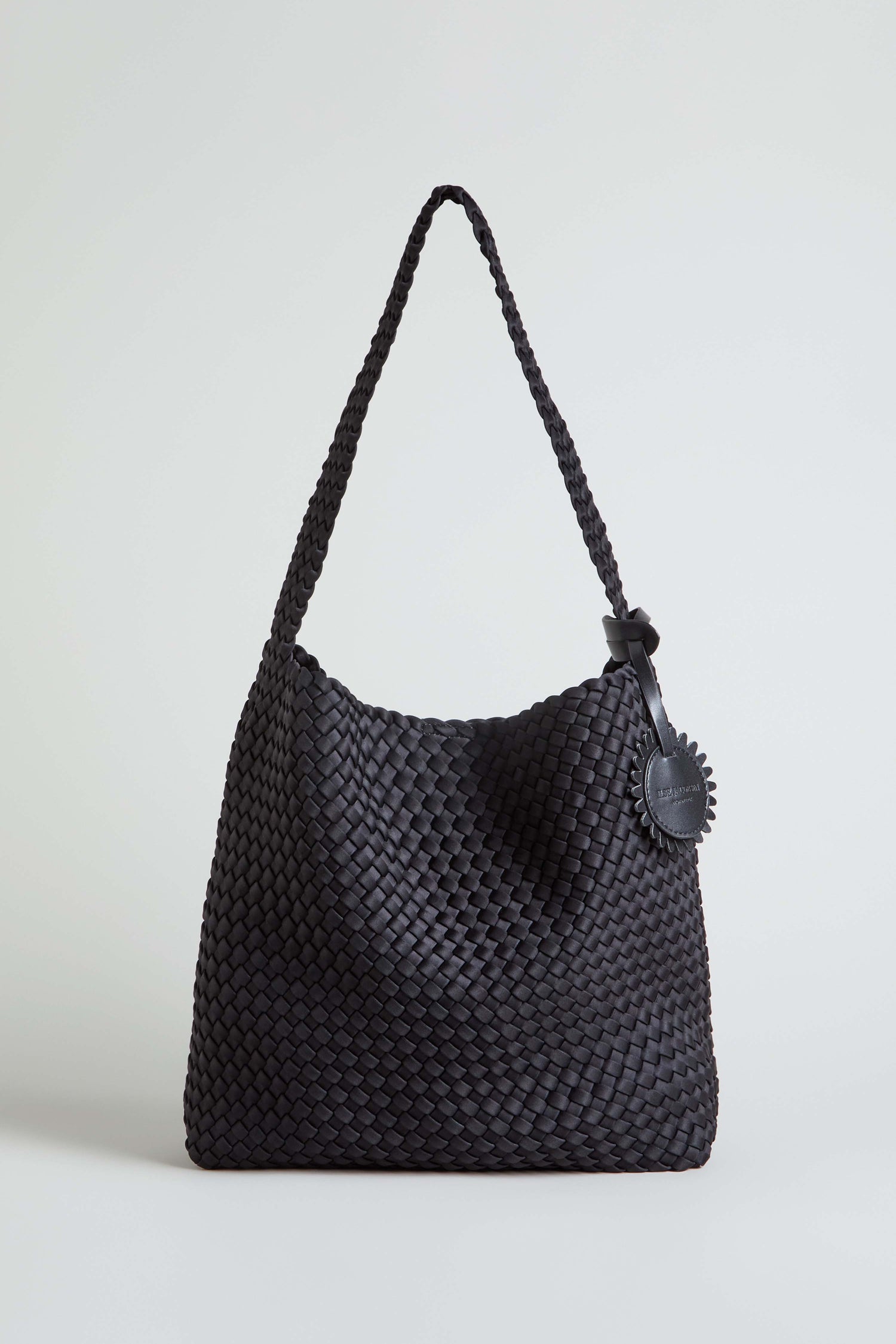 The Black Braided Shoulder Bag is shown upright against a plain light background, showcasing its woven construction, single strap, and round leather tag.
