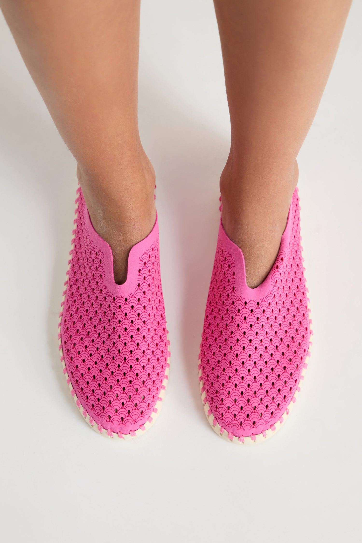 A person wearing Rose Tulip Slip on Shoes, celebrated for their lightweight comfort and perforated design, stands on a white surface.