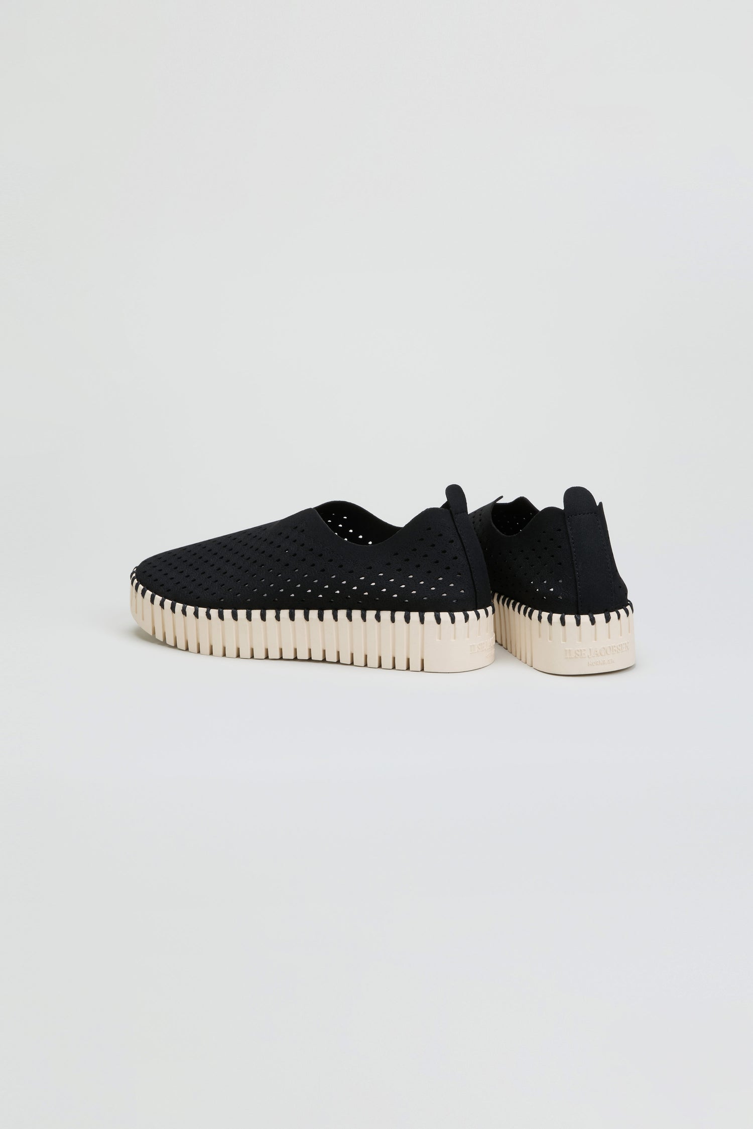 A pair of Tulip Platform Slip On Shoes in black, featuring a perforated design and white ribbed soles. Made from recycled microfiber for an eco-friendly touch, these breathable slip-on shoes are showcased against a plain light background.