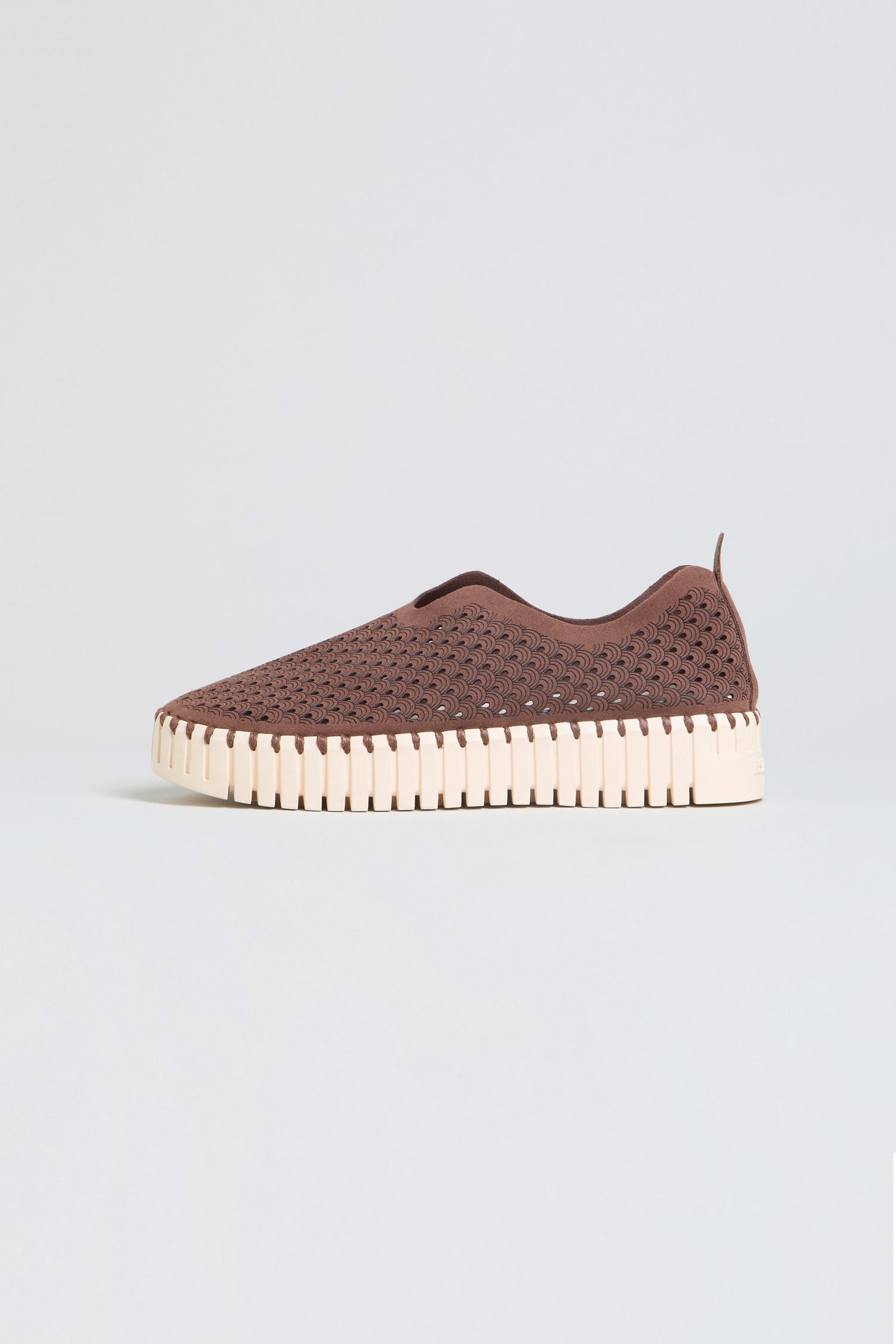The Tulip Platform Slip On Shoes in brown feature a perforated upper made from recycled microfiber and a white textured sole, providing a stylish and breathable slip-on option, showcased against a light gray background.