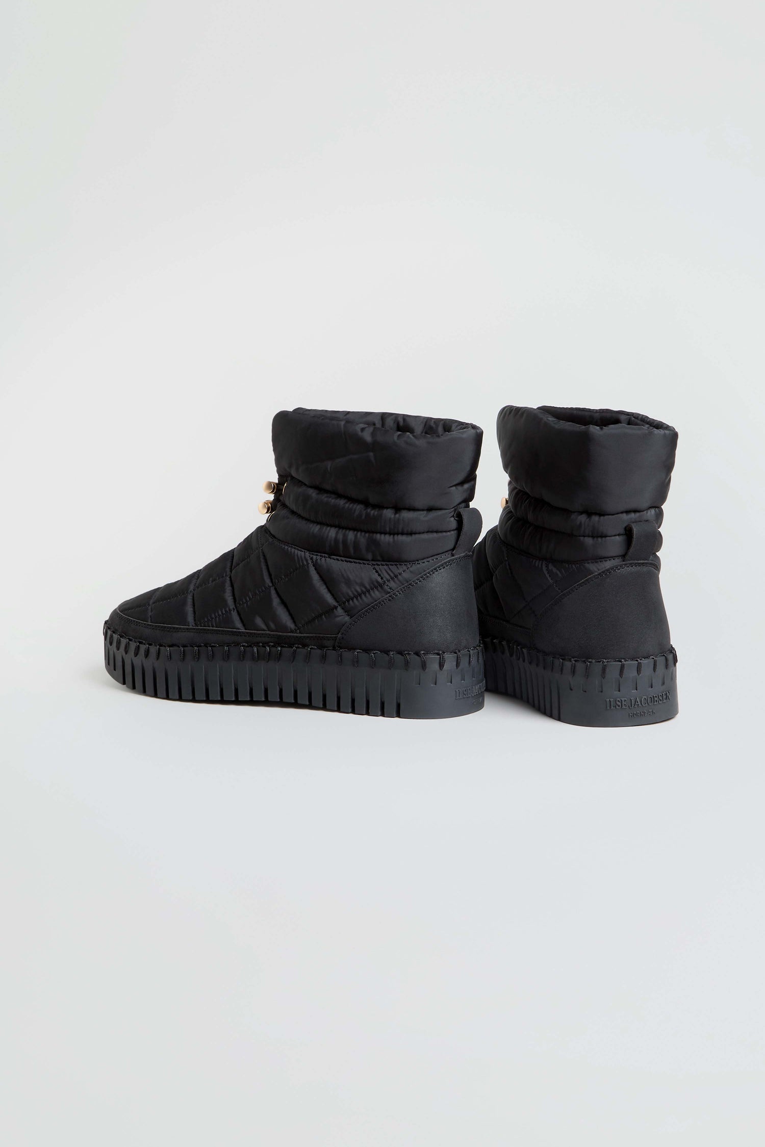 A pair of Tulip Quilted Winter Boots in black, featuring thick, cushioned soles and ridged tread, displayed from the back and side on a plain white background.