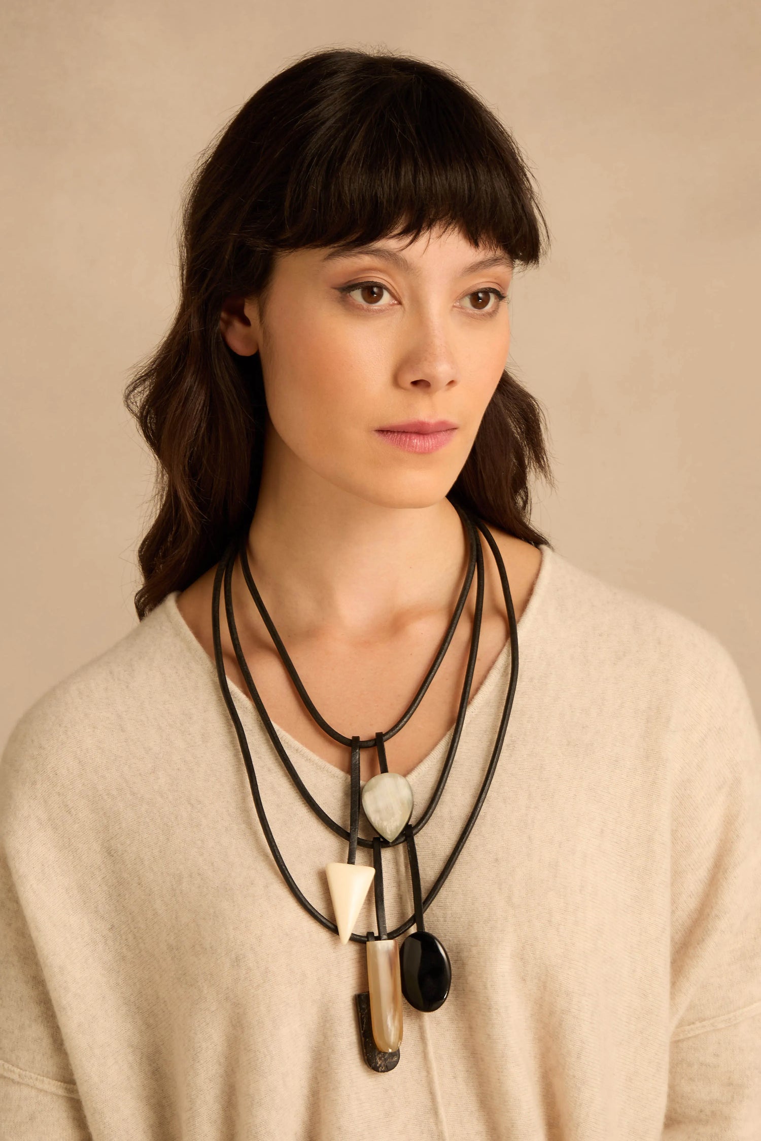 A woman wearing a Buffalo Horn Elements Necklace, a layered black cord statement piece featuring varied geometric pendants in black, white, and translucent horn-like materials.