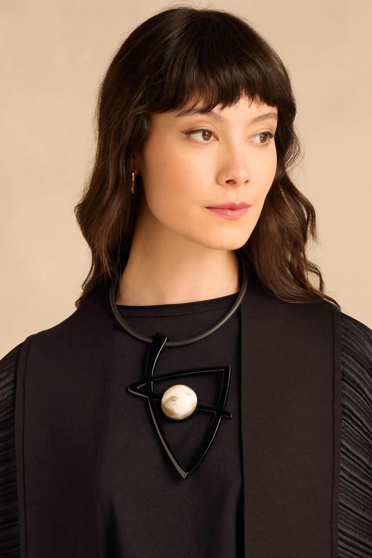 A person wears a Buffalo Horn & Resin Pendulum Necklace, featuring a large, black geometric pendant with a round, mottled light-colored stone center.