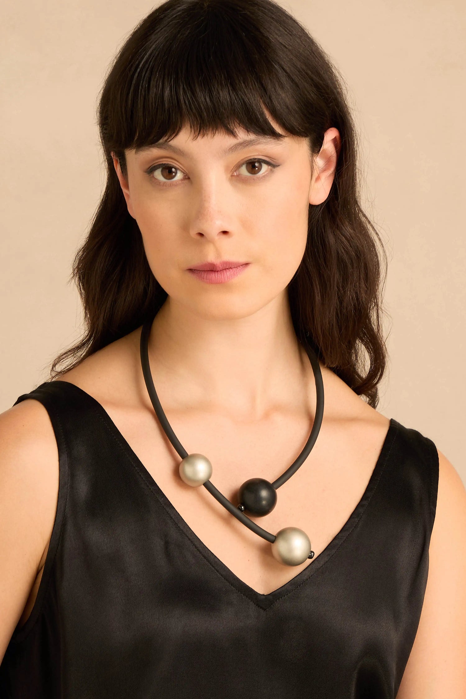 A person wearing a Triple Sphere Statement Necklace featuring a black cord strung with two metallic spheres and one matte black sphere.
