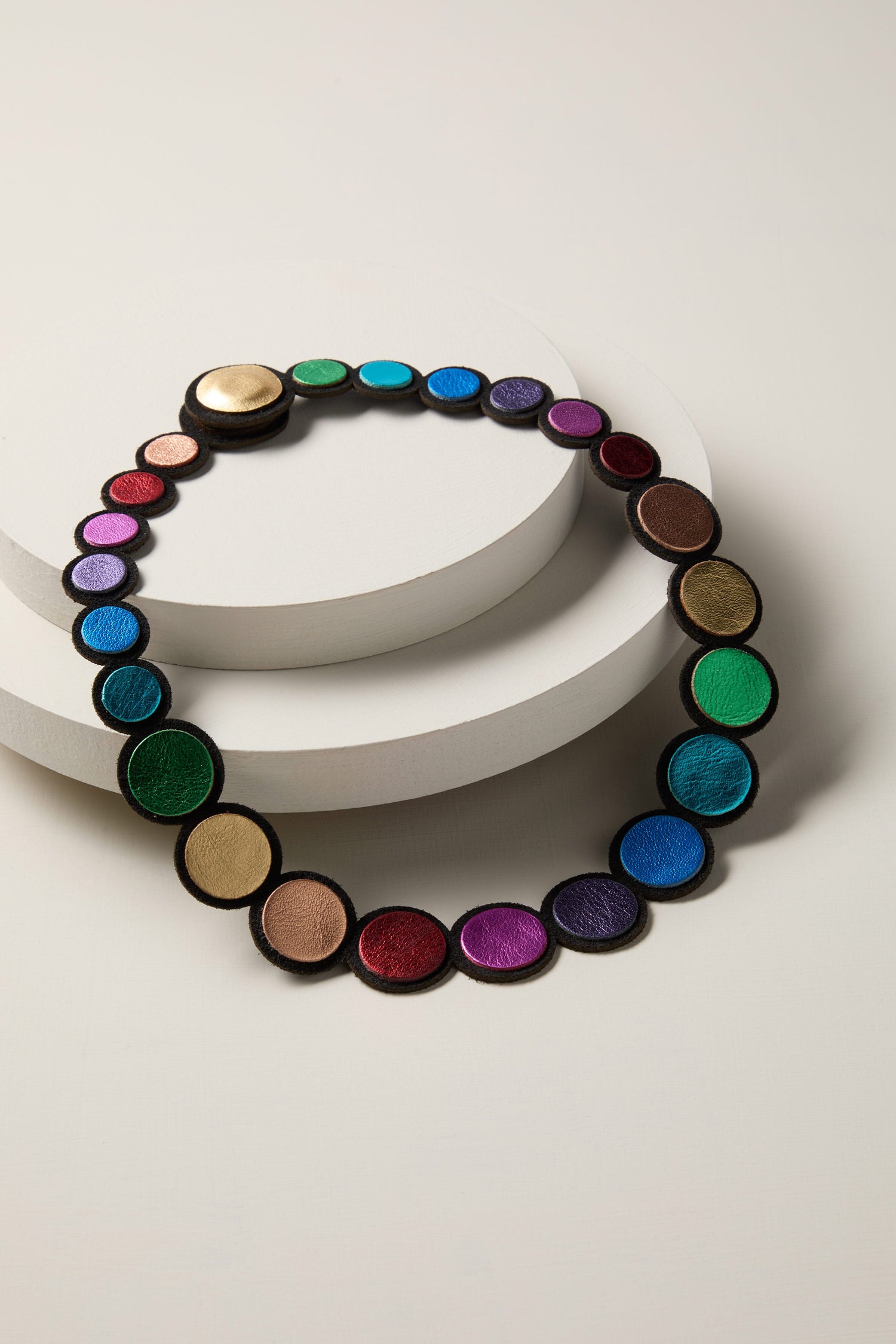 A vibrant, multi-colored Metallic Rainbow Leather Disc Necklace on a white surface.