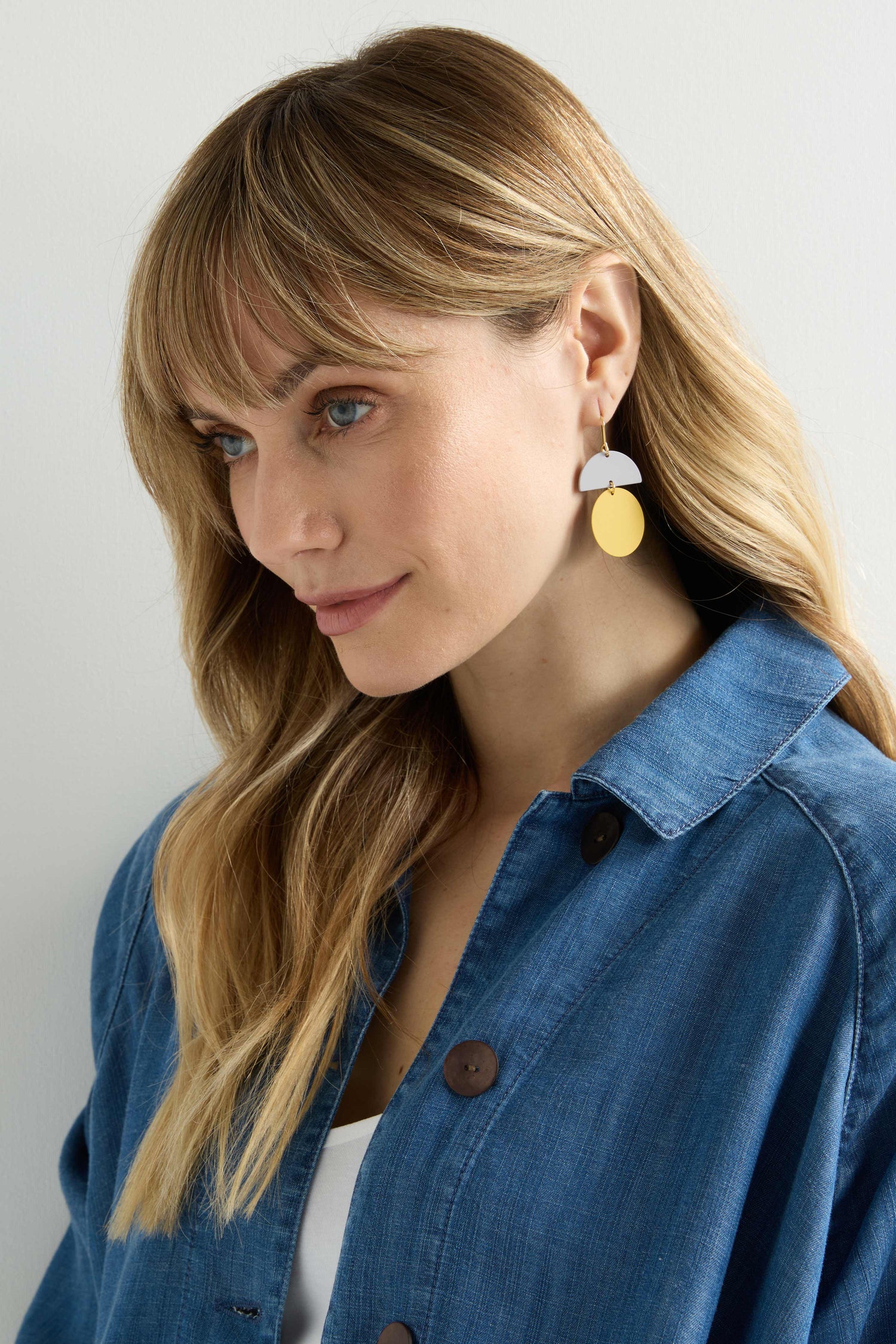 A woman with long blonde hair in a blue denim shirt and Colour Pop Circle Drop Earrings gazes to the side against a plain background.