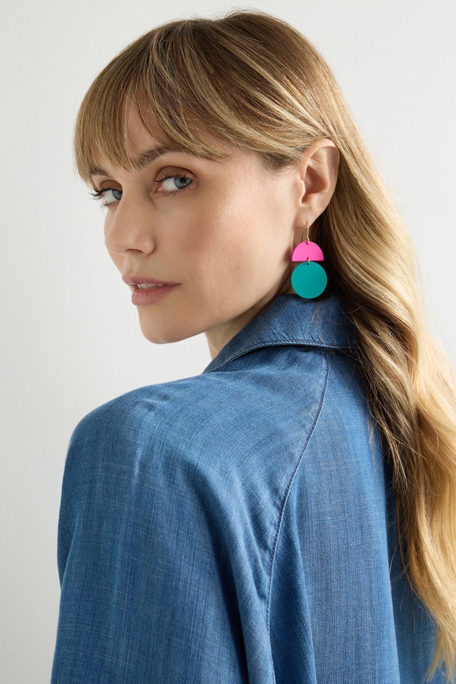 A woman with long hair in a blue denim jacket looks over her shoulder, making a statement with vibrant Colour Pop Circle Drop Earrings.