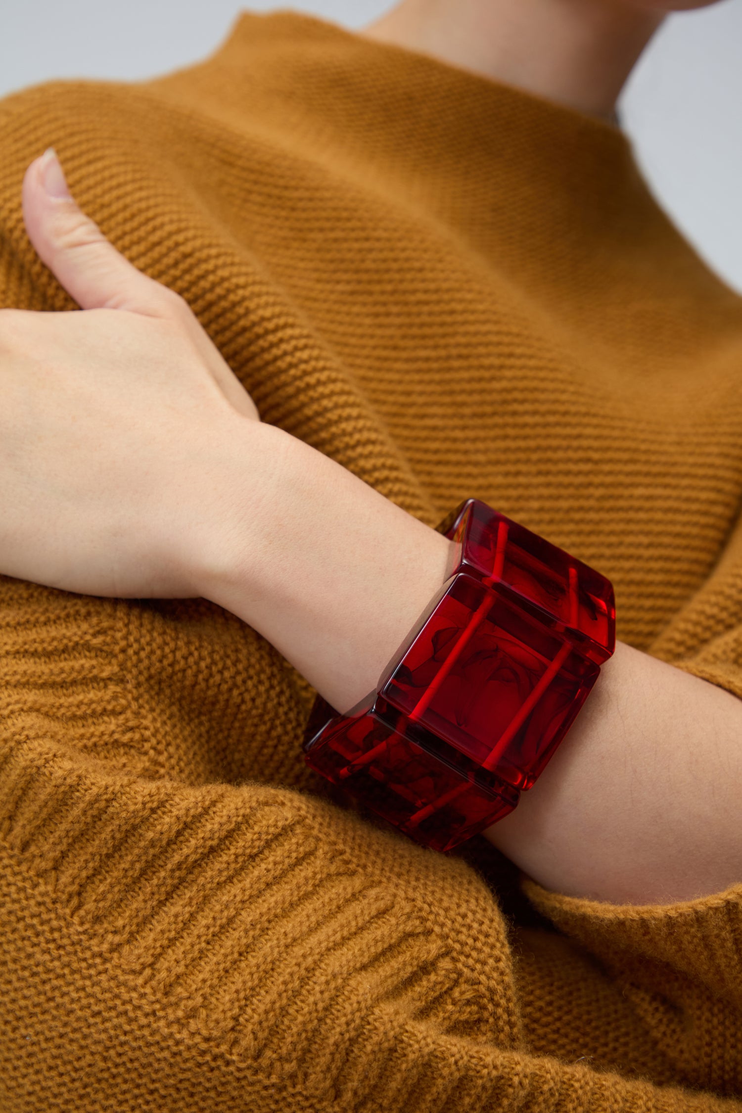 A person wears a textured brown sweater and a large, translucent Ruby Resin Bracelet, highlighting sustainable resin jewellery.