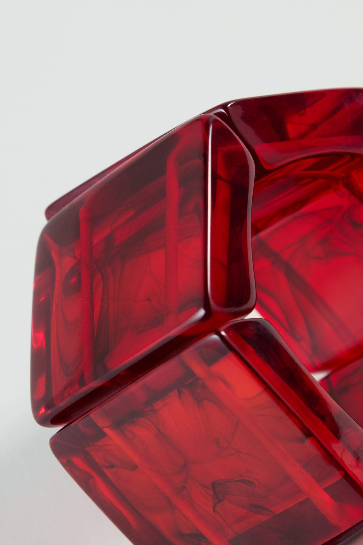 Close-up of a glossy, translucent red geometric object with square panels and marbled patterns—reminiscent of the Ruby Resin Bracelet, known for bold, sustainable resin jewellery—set against a plain background.