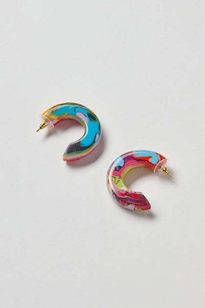 The Kandinsky Hoop Earrings feature two crescent-shaped resin hoops with a marbled blue, pink, yellow, and green pattern, set on a white background.