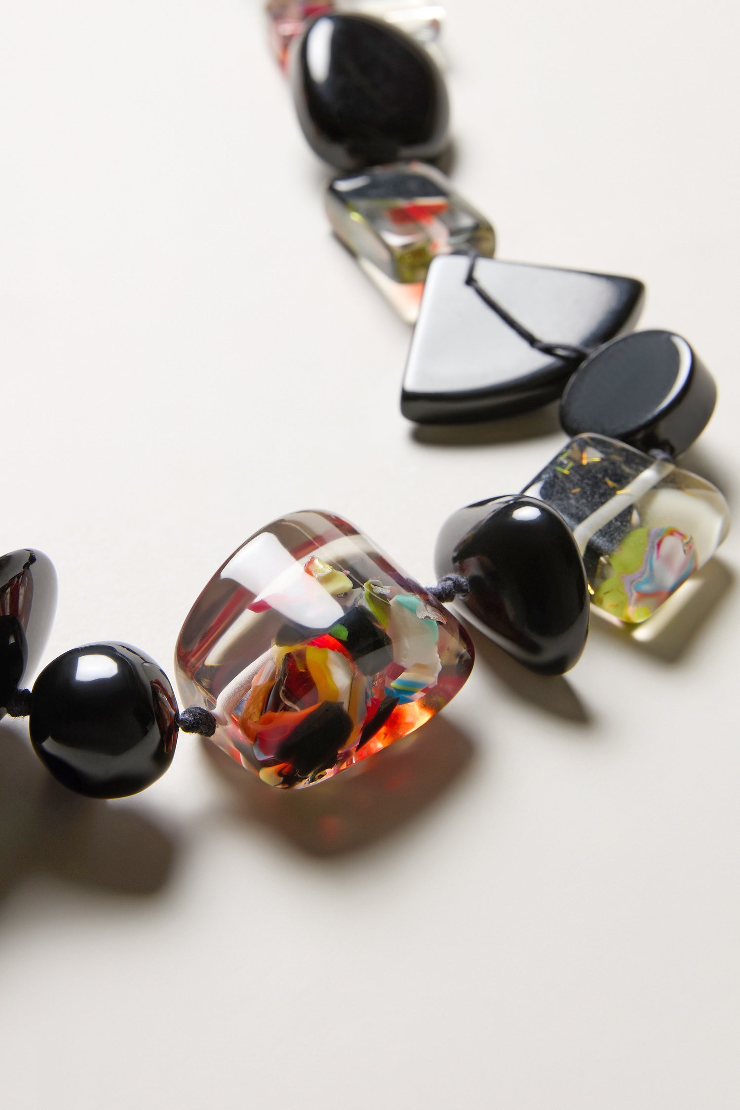 A close-up view of the Short Multi Shapes Resin Necklace, a handcrafted piece featuring large, uniquely shaped black and glass resin beads displayed on a light background.