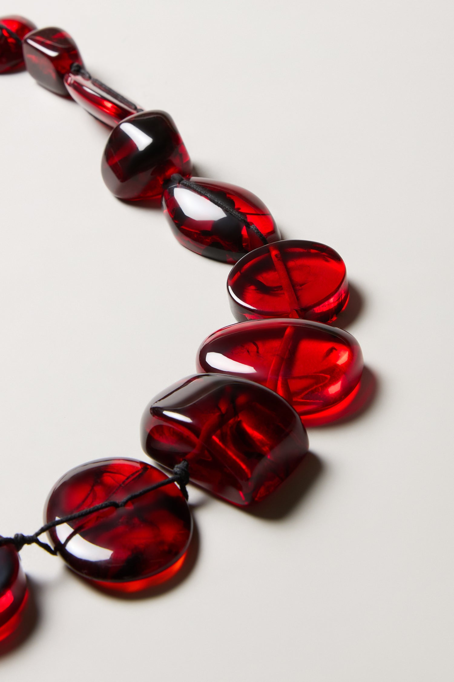 A close-up of the Ruby Resin Bead Necklace, featuring large, irregular red translucent beads. This handmade piece adds an artisanal touch to any look.