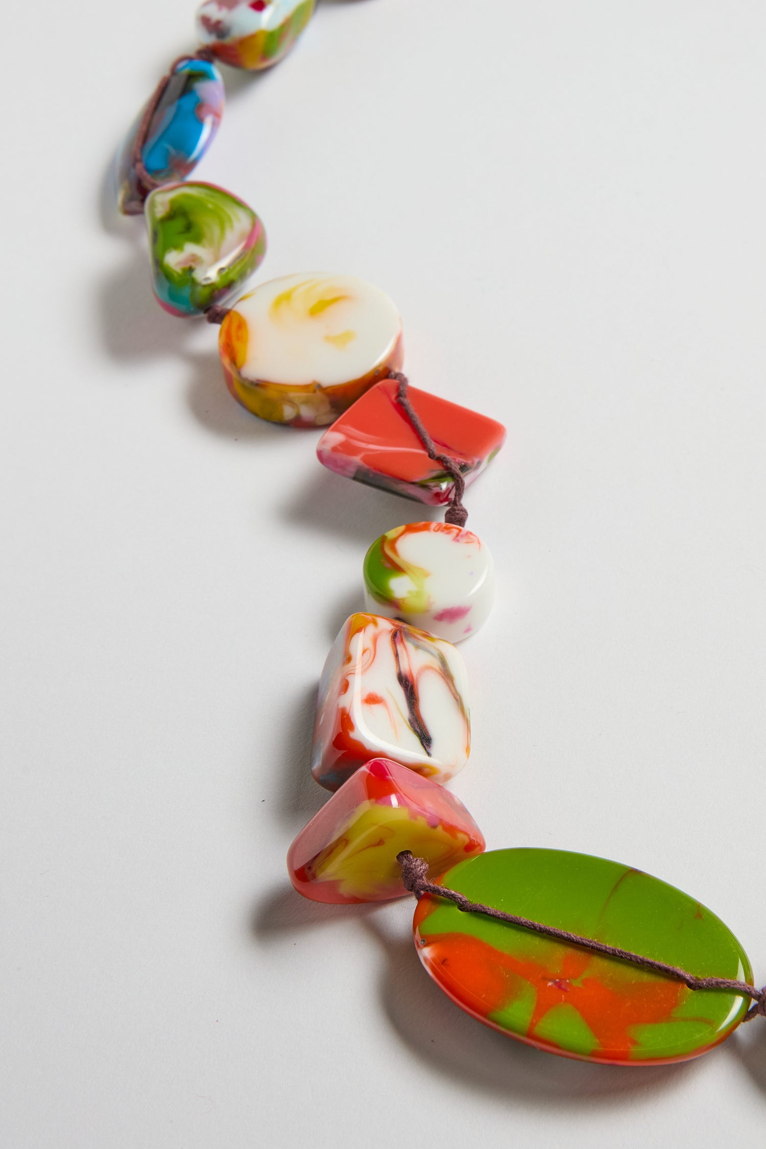 A close-up of the Long Kandinsky Pebble Resin Necklace displays its colorful, handcrafted marbled shapes and sculptural design against a white background.