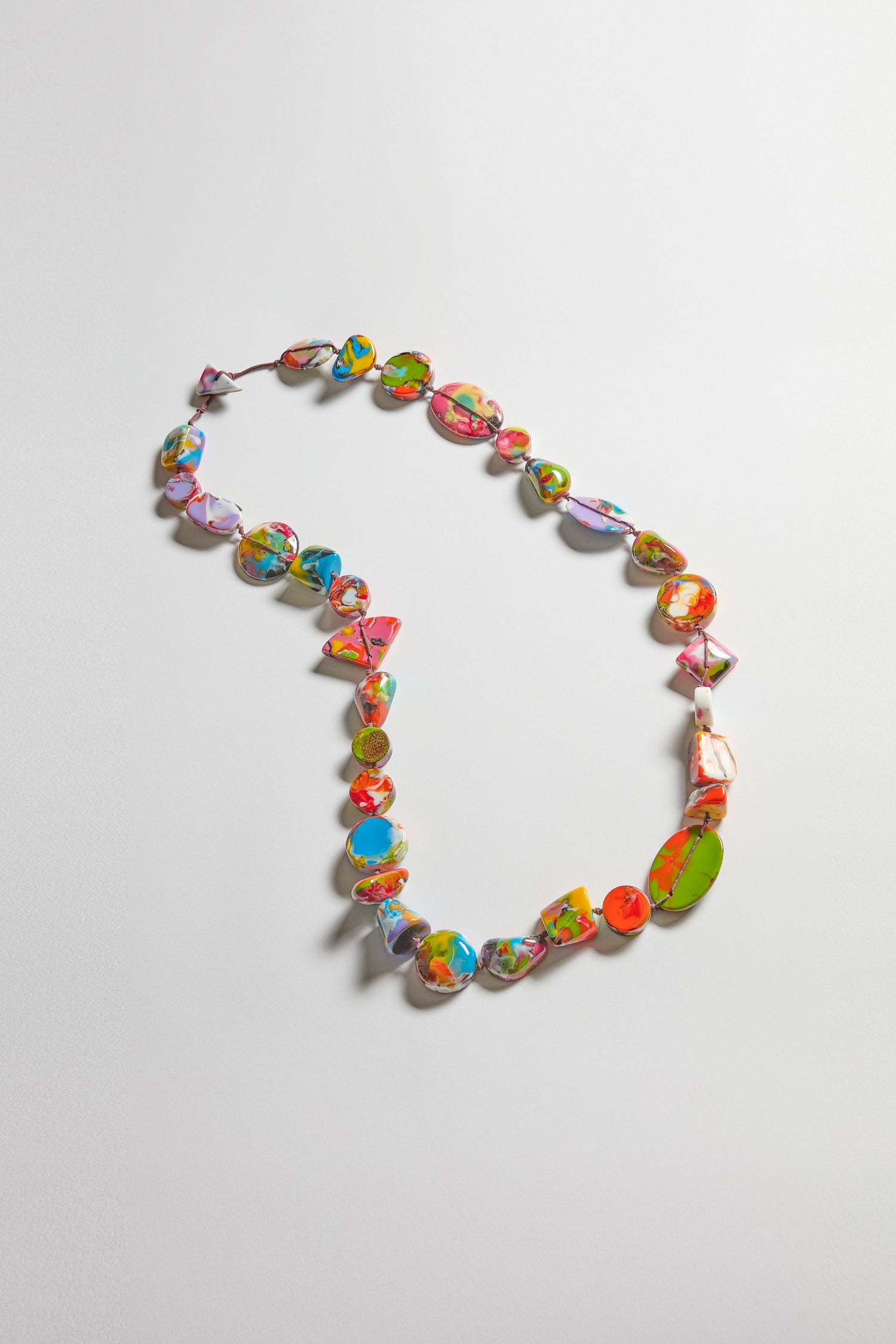 The Long Kandinsky Pebble Resin Necklace is handcrafted with irregular, multicolored resin beads arranged in an oval on a plain light background.