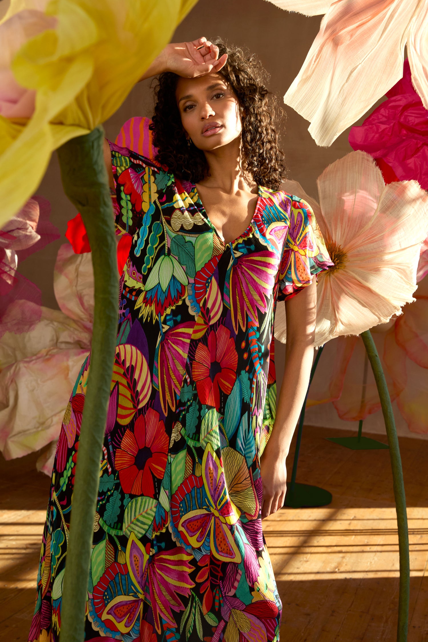 A woman wears the Fantasy Forest Georgette Bubble Dress in a relaxed, oversized fit indoors, surrounded by oversized artificial tropical plants as sunlight brightens the vivid scene.