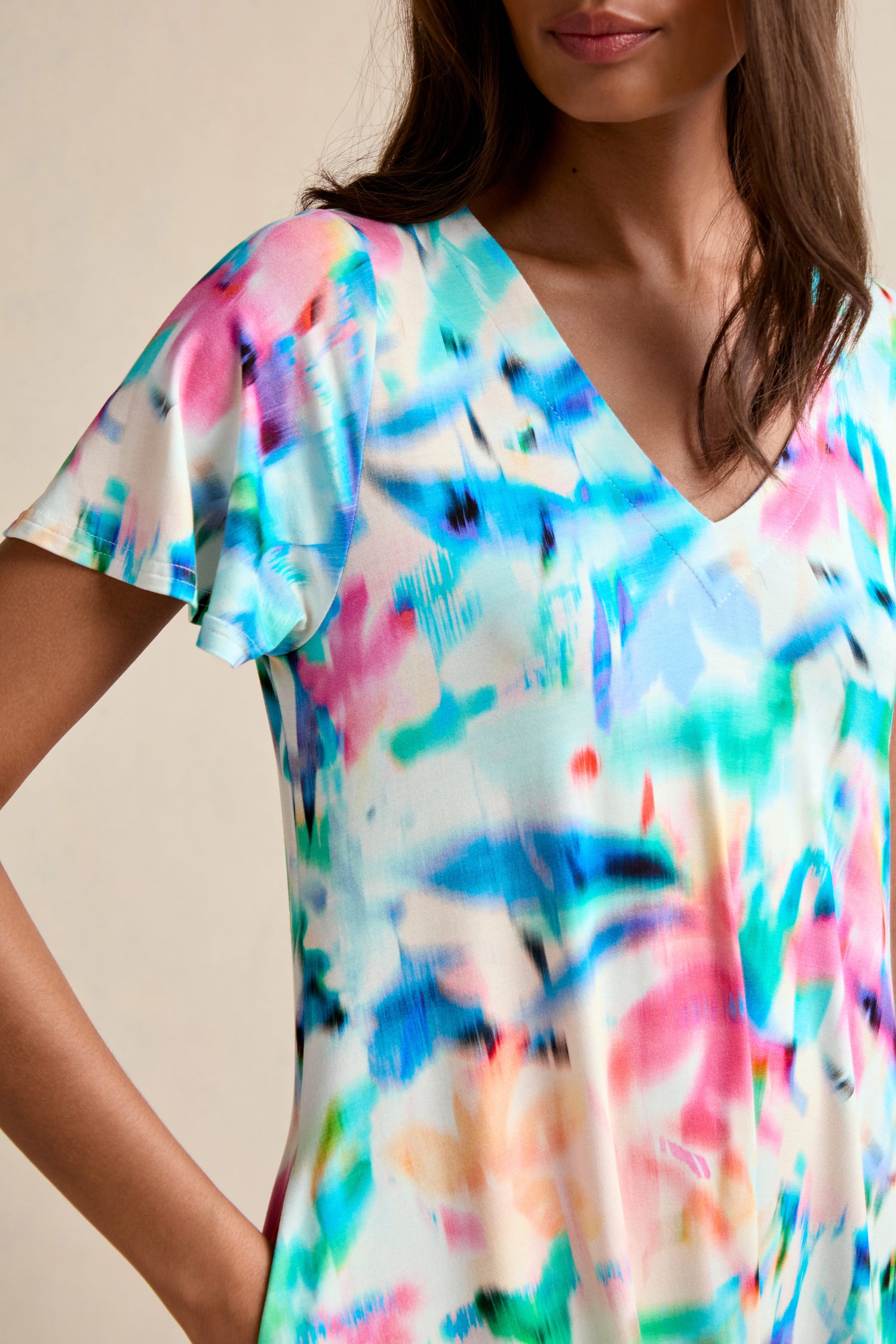 A person wears the Petal Haze Jersey Flare Dress, a short-sleeve V-neck style featuring a colorful abstract pattern in blue, pink, and green.