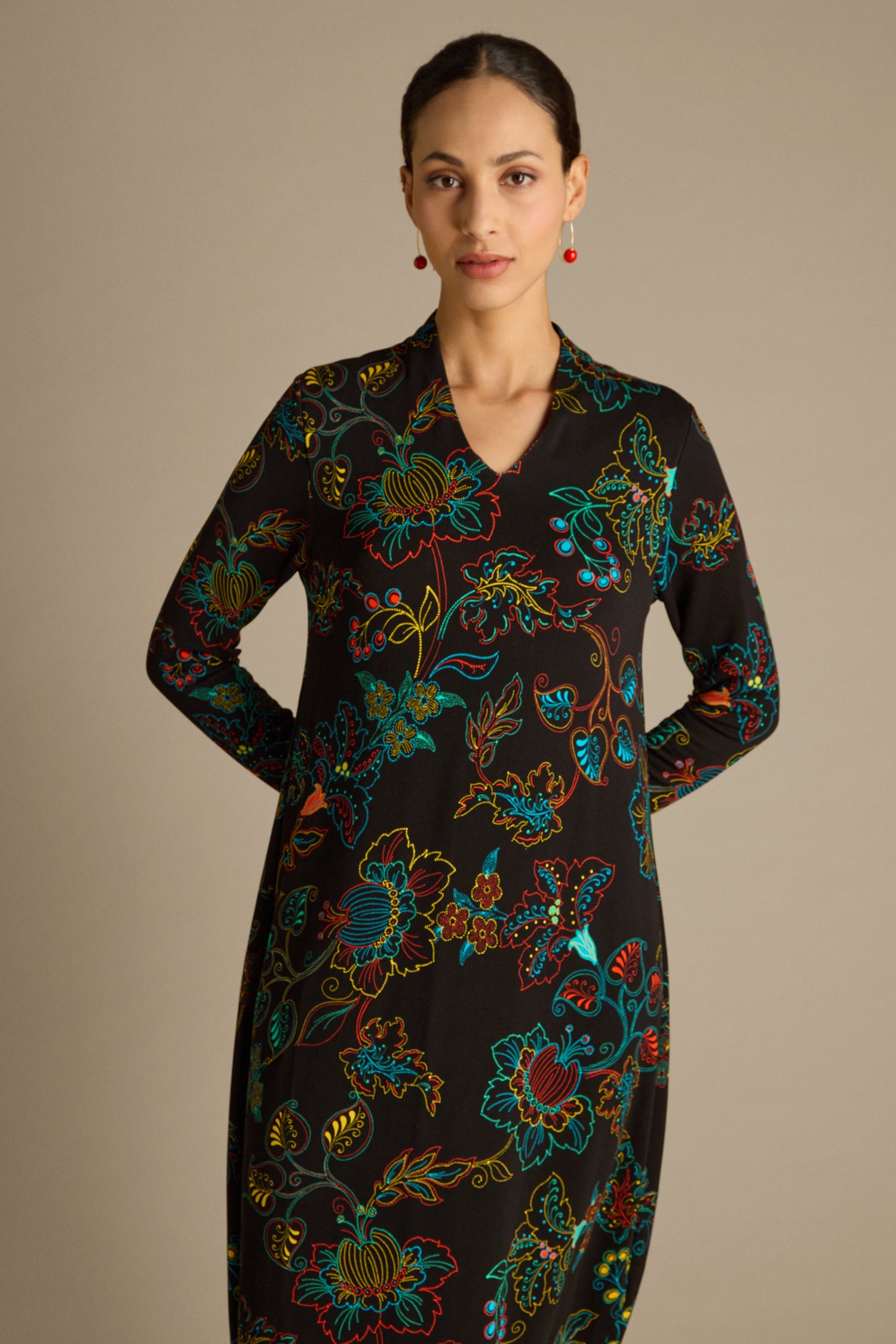 A person stands against a neutral background, wearing the Bright Dotted Floral Jersey Dress with a V-neckline. The warm-handle jersey fabric drapes elegantly, accentuating the vibrant patterns.