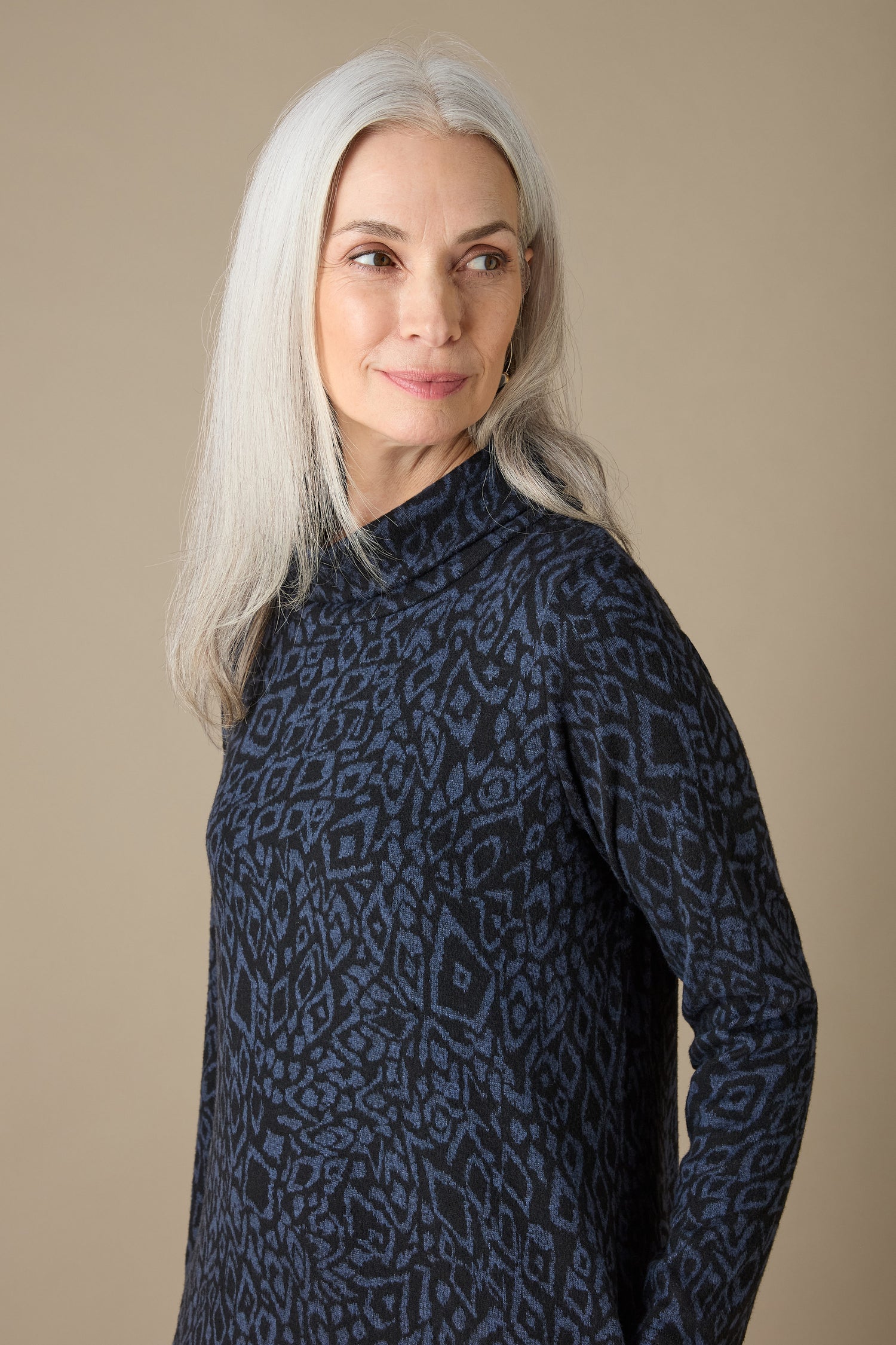 A person with long gray hair, clad in an Ikat Soft Jersey Bubble Dress featuring an abstract print pattern, stands against a plain background, looking to the side and creating a unique silhouette.