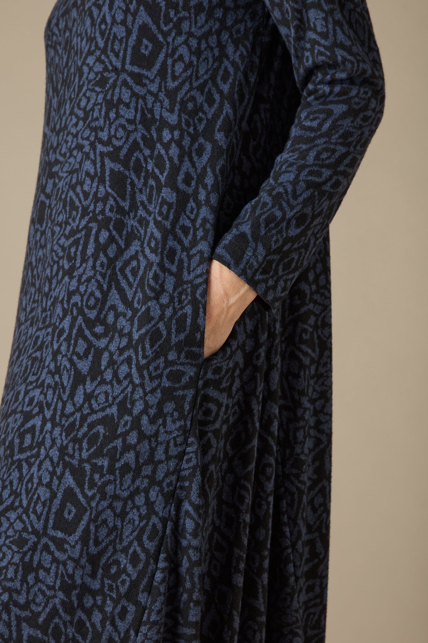 A close-up features an individual wearing the Ikat Soft Jersey Bubble Dress, displaying its abstract print in blue and black. Their hand casually nestled in the side pocket emphasizes the dress's distinctive silhouette.