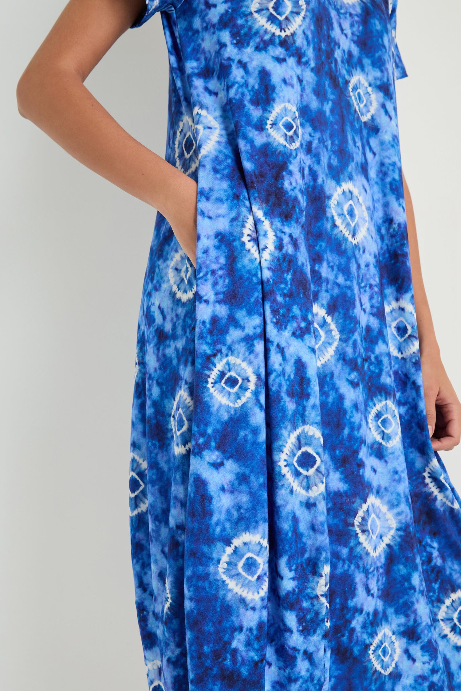 Model wears the Tie Dye Circles Jersey Bubble Dress, made from viscose stretch jersey in blue and white tie-dye, with a hand in the pocket, standing against a plain light background.