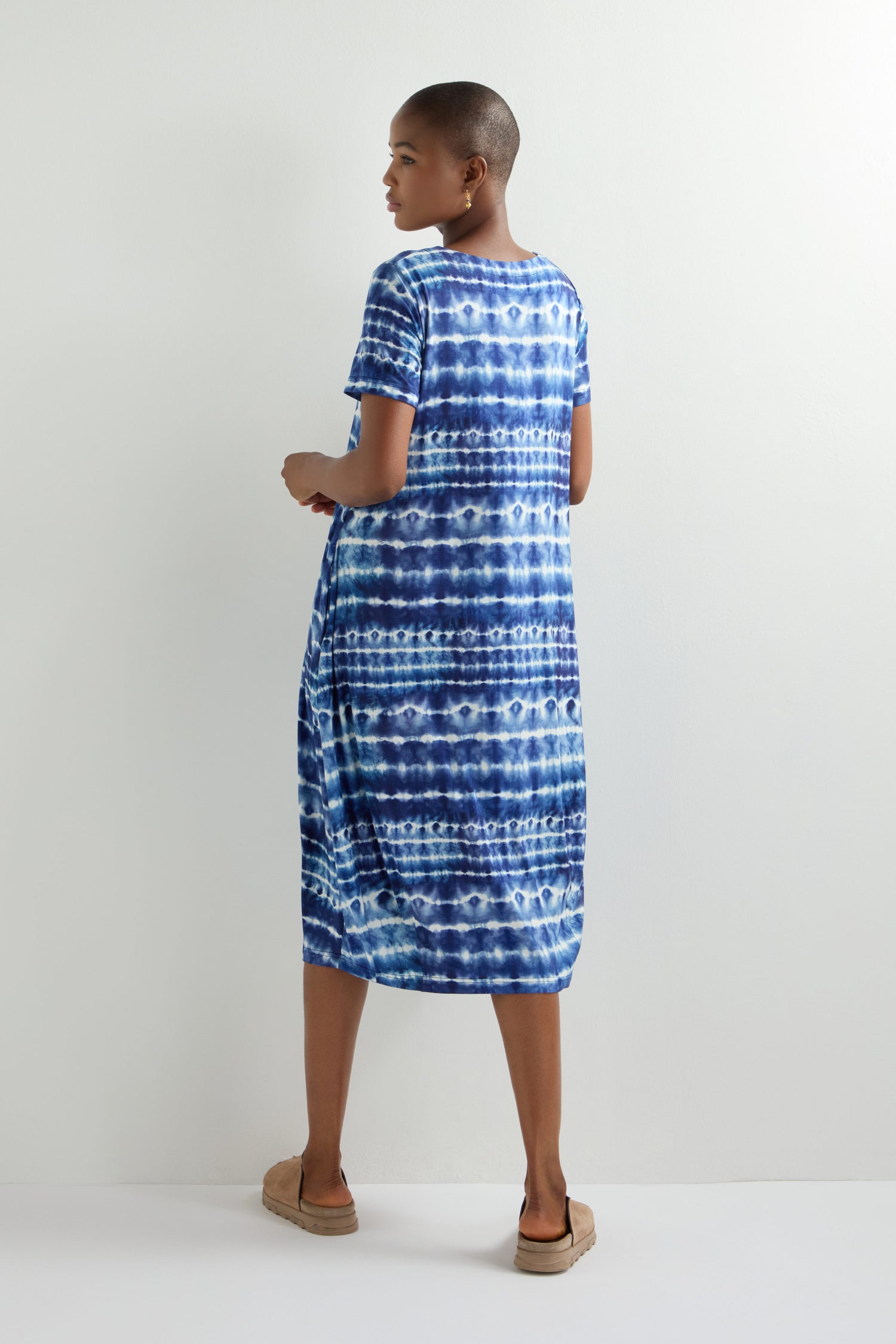 A person models the effortless style of a Tie Dye Jersey Bubble Dress in blue and white against a plain white background, captured from the side and back.