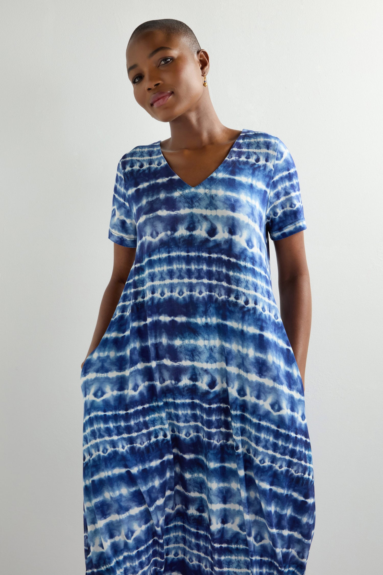 Wearing a classic fit Tie Dye Jersey Bubble Dress in blue and white with a V-neck, this midi dress features pockets and stands out elegantly against the plain background.