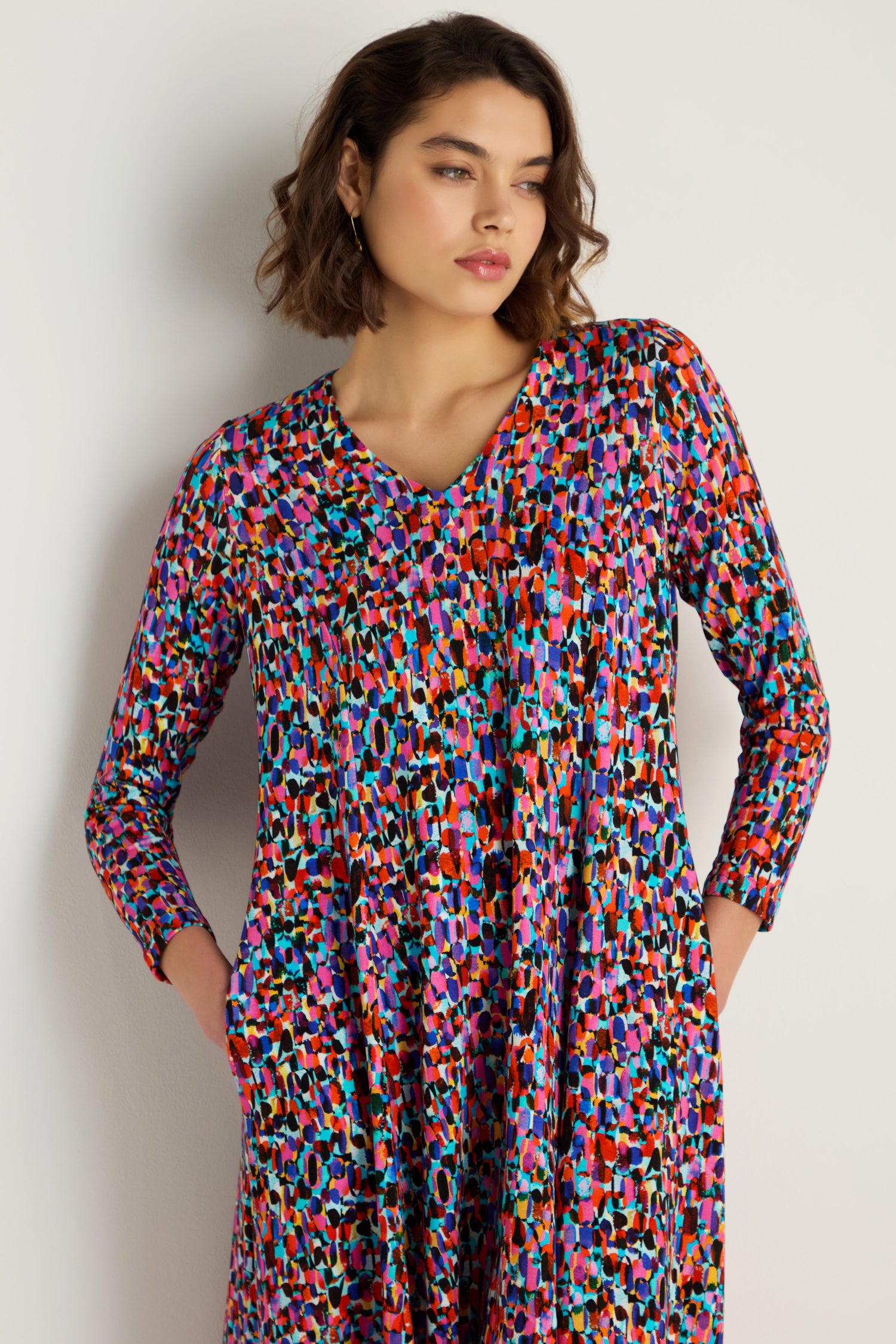 Woman models the Painted Spots Jersey Flared Dress—midi length with multicolored abstract spots and pockets—standing against a plain, light background.