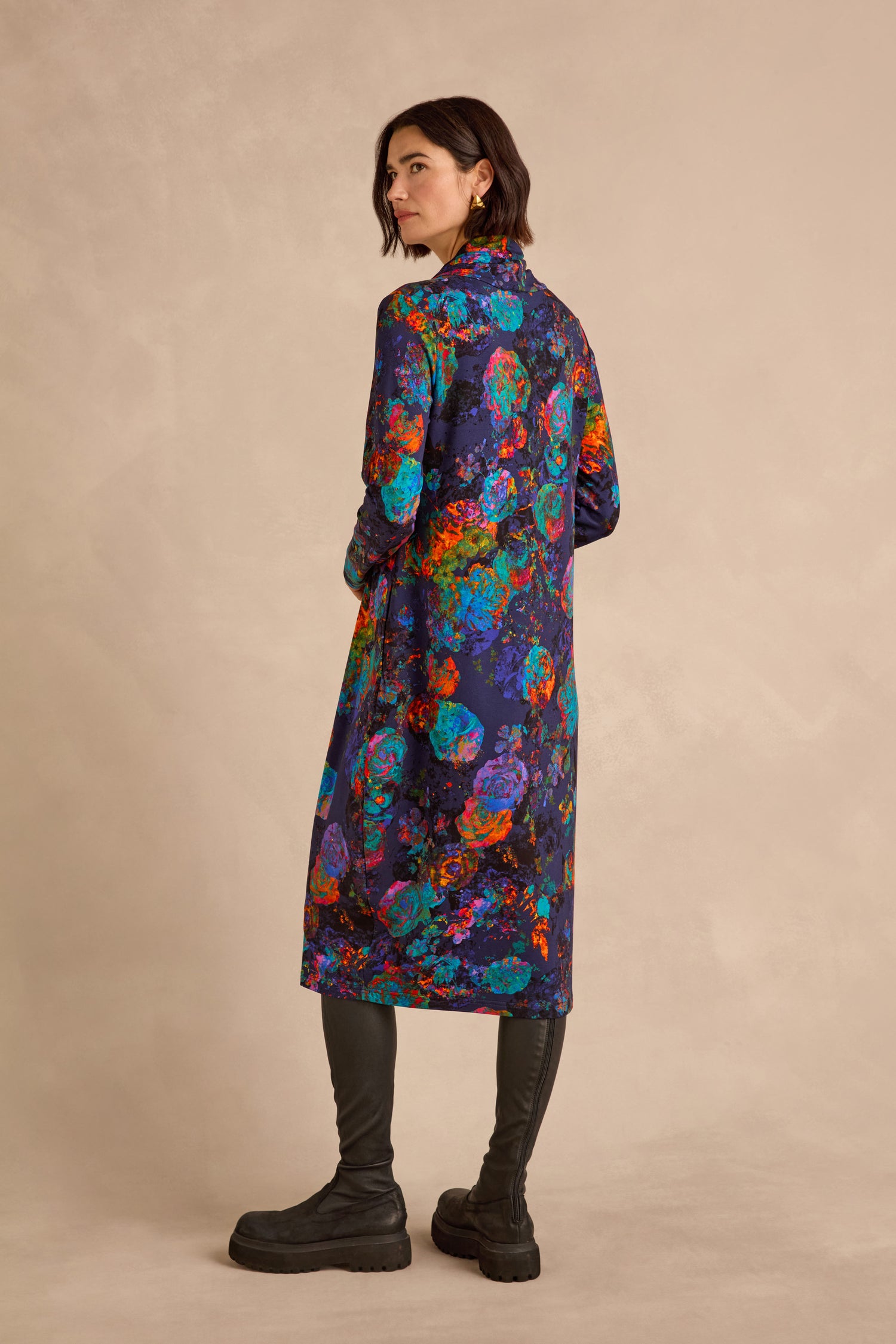 A woman stands in profile against a neutral background, wearing the Midnight Floral Jersey Bubble Dress and tall black boots.