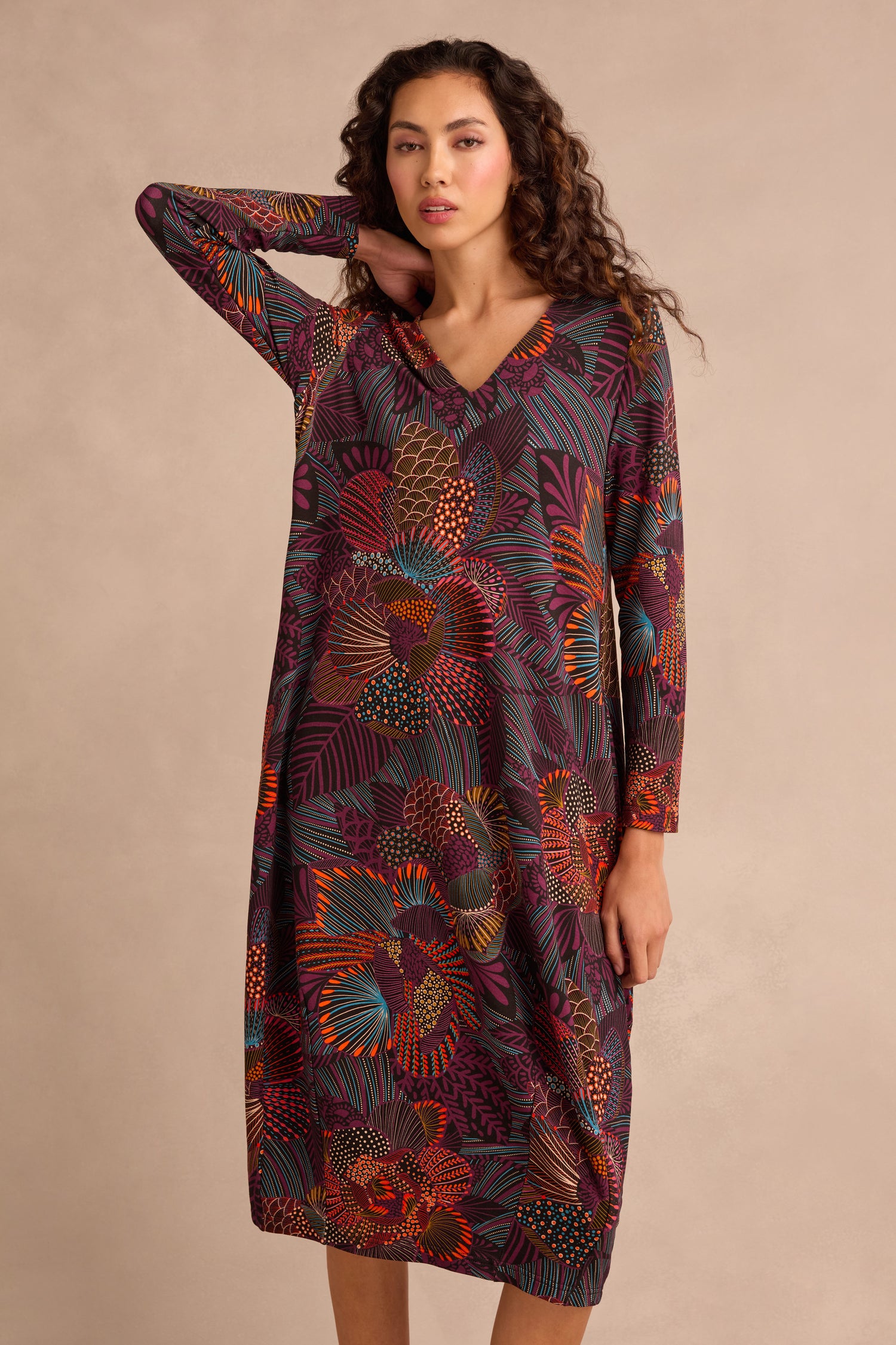 A person wearing the Abstract Linear Floral Jersey Bubble Dress, featuring long sleeves and a colorful floral pattern, stands against a neutral background with one hand touching their head.