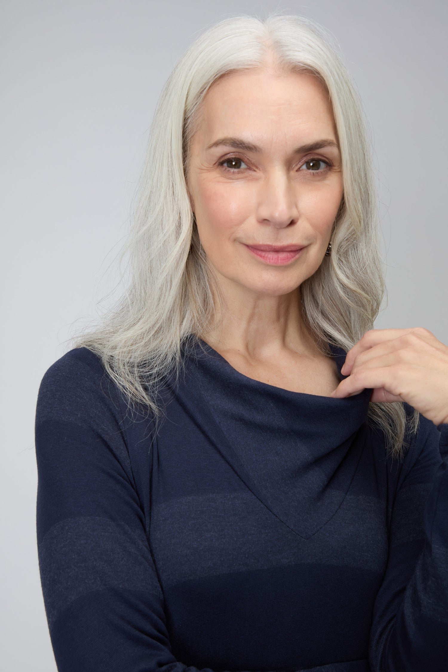An older woman with long gray hair wears the Soft Viscose Jersey Stripe Dress in navy blue, standing against a plain light background and looking at the camera with a slight smile.