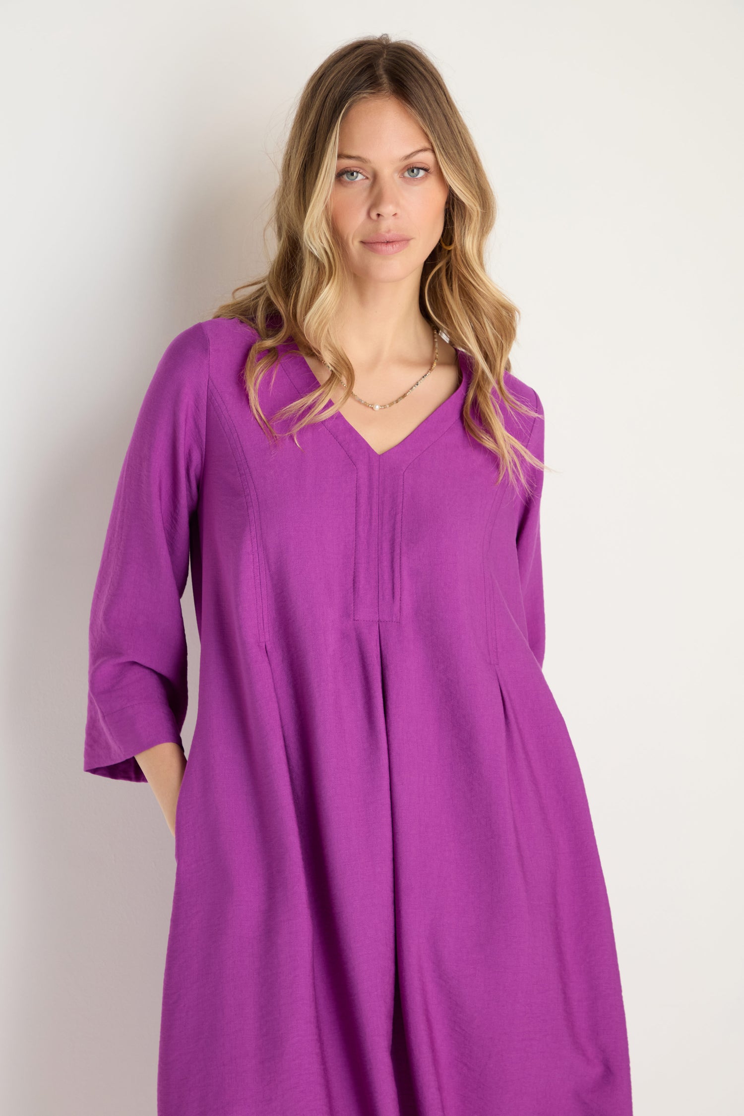 A woman with long blonde hair wears the Textured Viscose Bubble Dress in orchid purple, featuring a loose fit, long sleeves, V-neckline, and textured fabric, standing against a plain light background.
