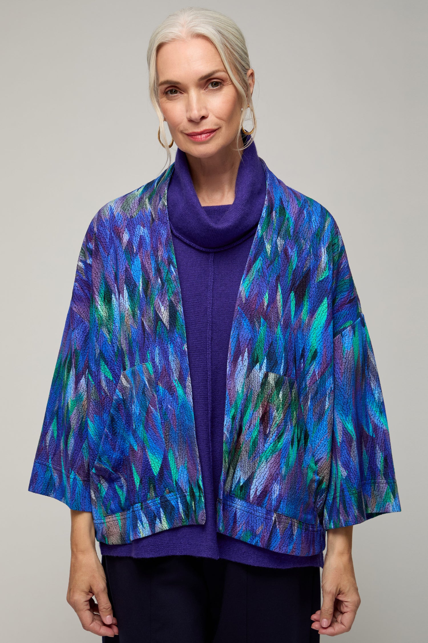 An older woman with gray hair, wearing a purple top and the Abstract Feather Jersey Jacket, stands against a plain background.