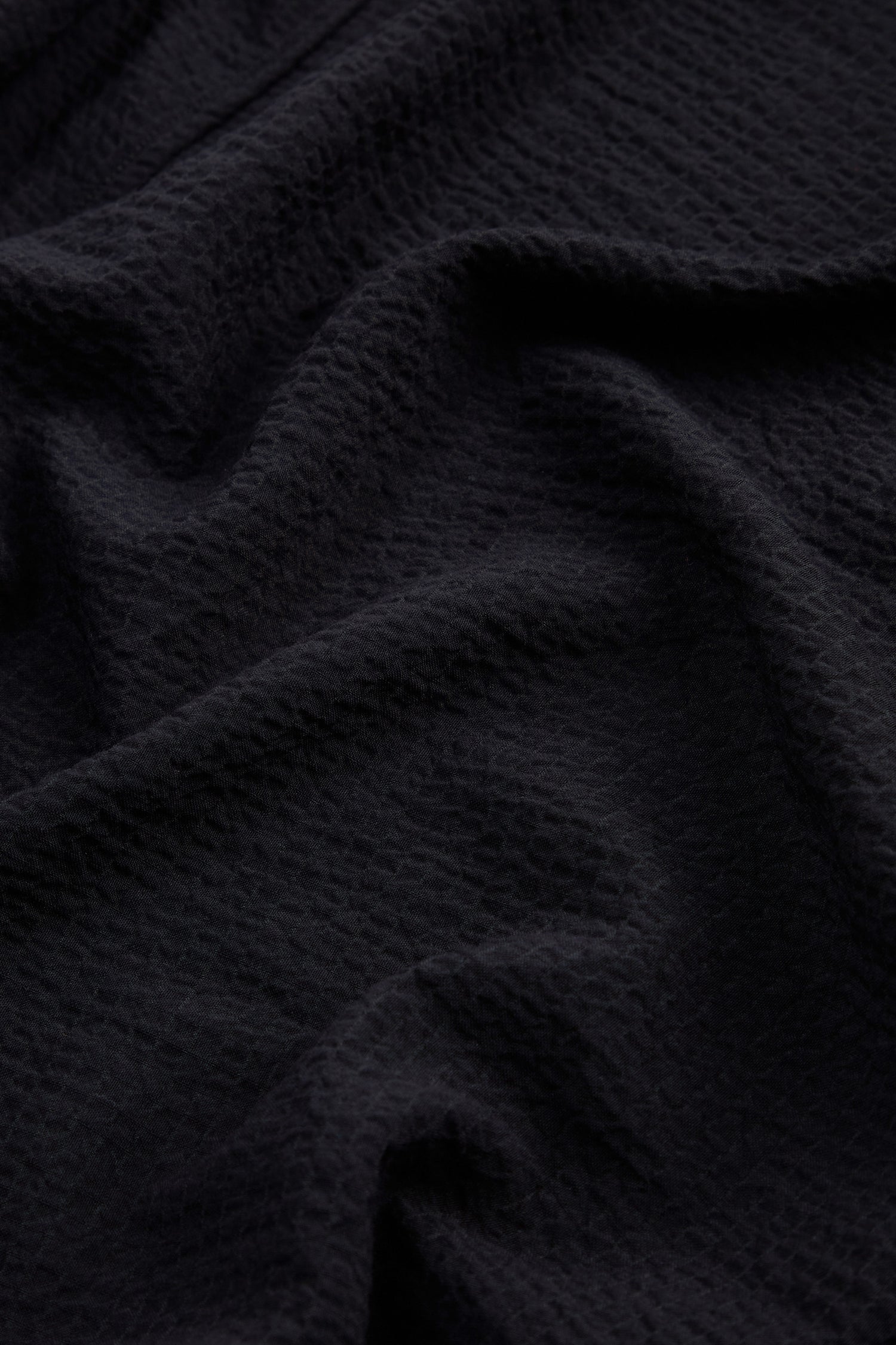 Close-up of a dark, textured fabric with visible folds and a slightly wrinkled surface, reminiscent of the Mini Crinkle Viscose Wide Leg Trouser.