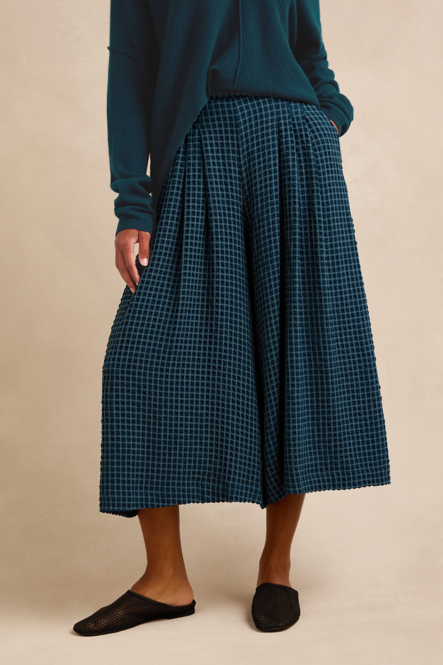 Person wearing a teal long-sleeve top and Seersucker Squares Wide Trousers, paired with black slip-on shoes, standing against a beige background.