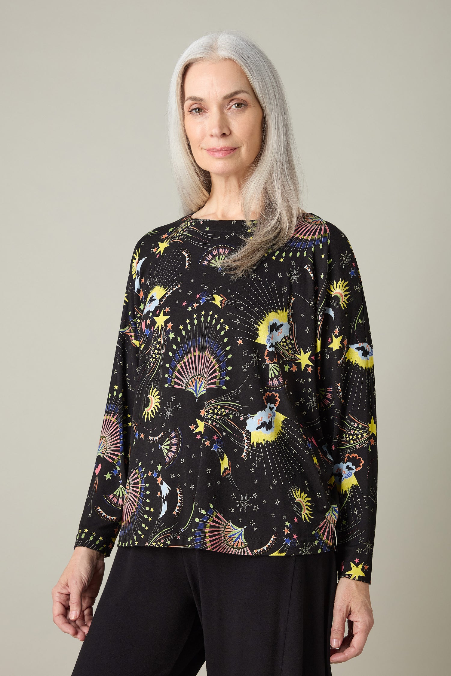 A woman with long gray hair is wearing the Celestial Dreams Jersey Boxy Top, featuring a colorful celestial print, against a plain background.